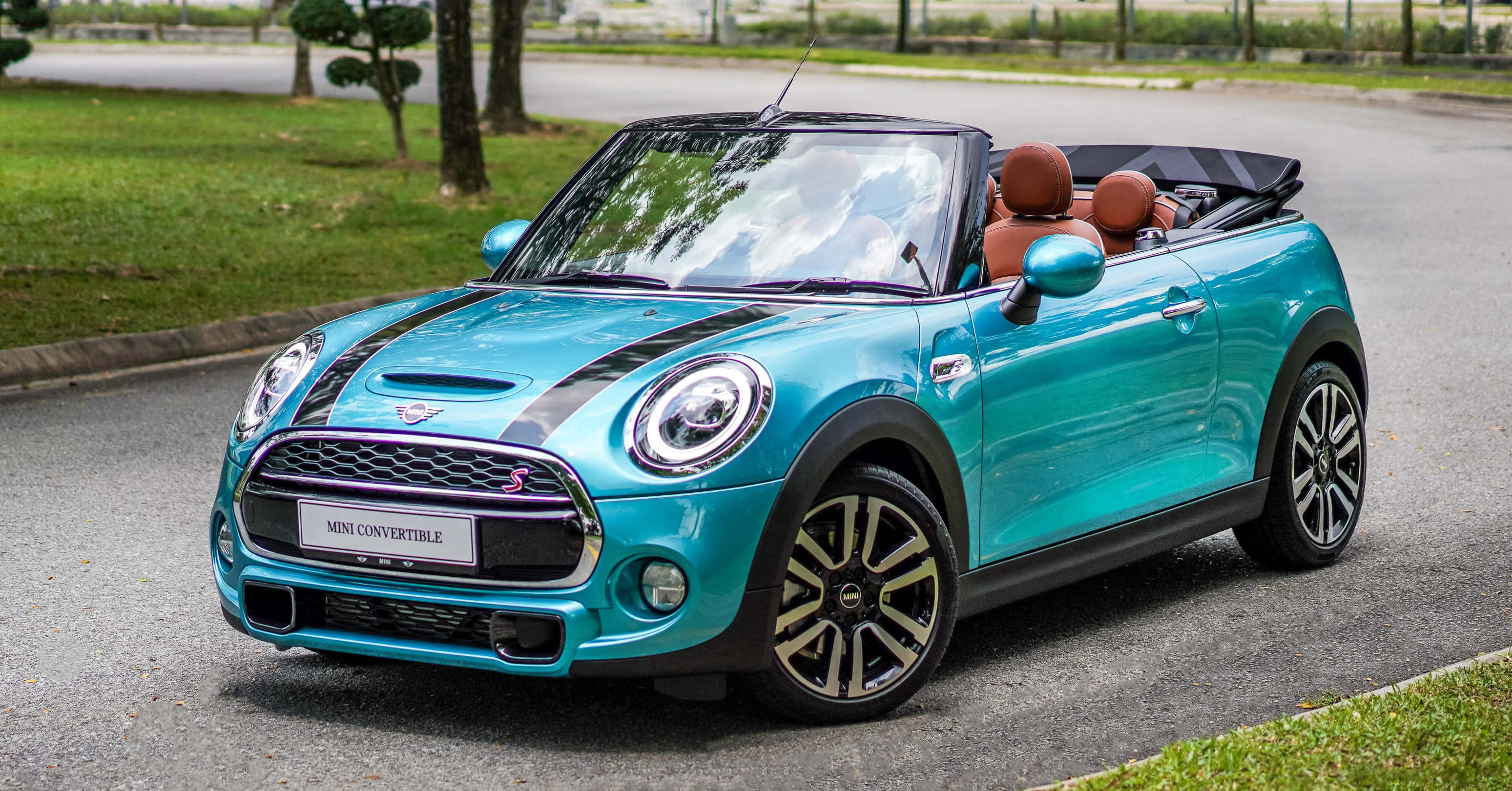 Mini Cooper Convertible 桌布 壁紙 — 一輛充滿活力的青綠色MINI Convertible，帶有黑色賽車條紋，停在鋪砌的道路上，旁邊是綠草和樹木。