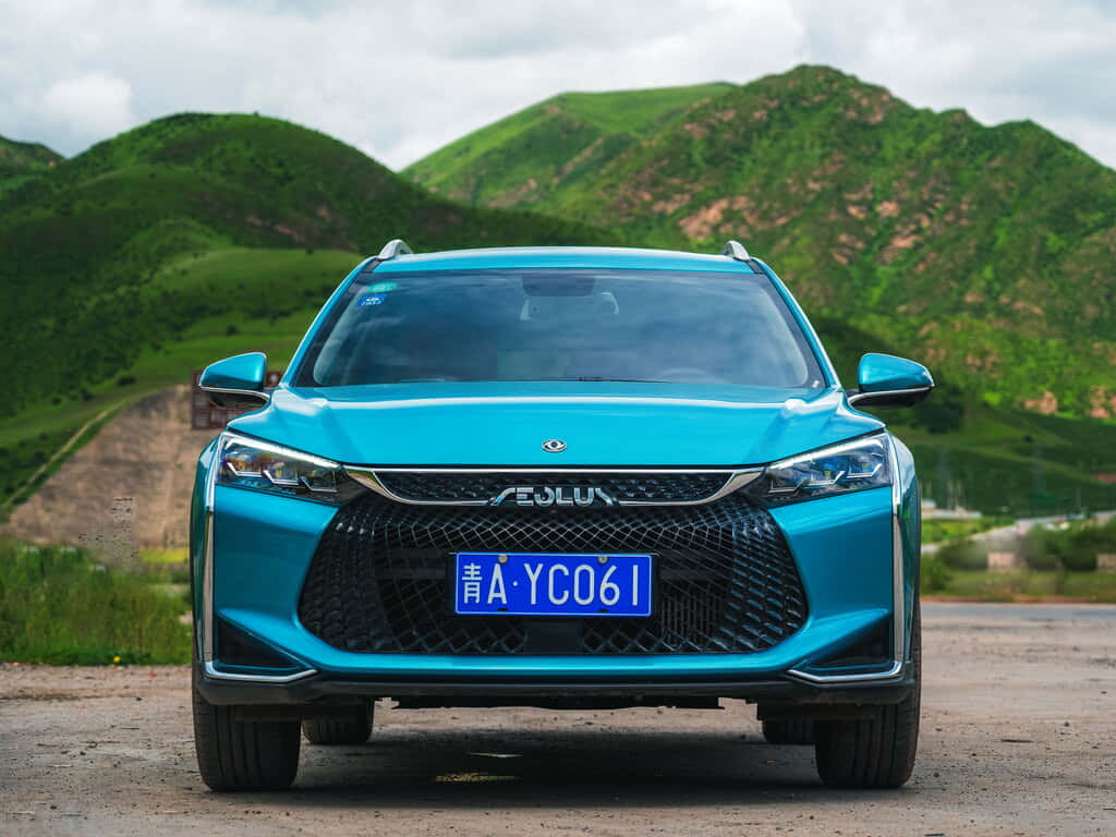  壁紙 — 一輛充滿活力的藍綠色SUV在泥土路上向前行駛，背景是茂密的綠色山丘和陰天。
