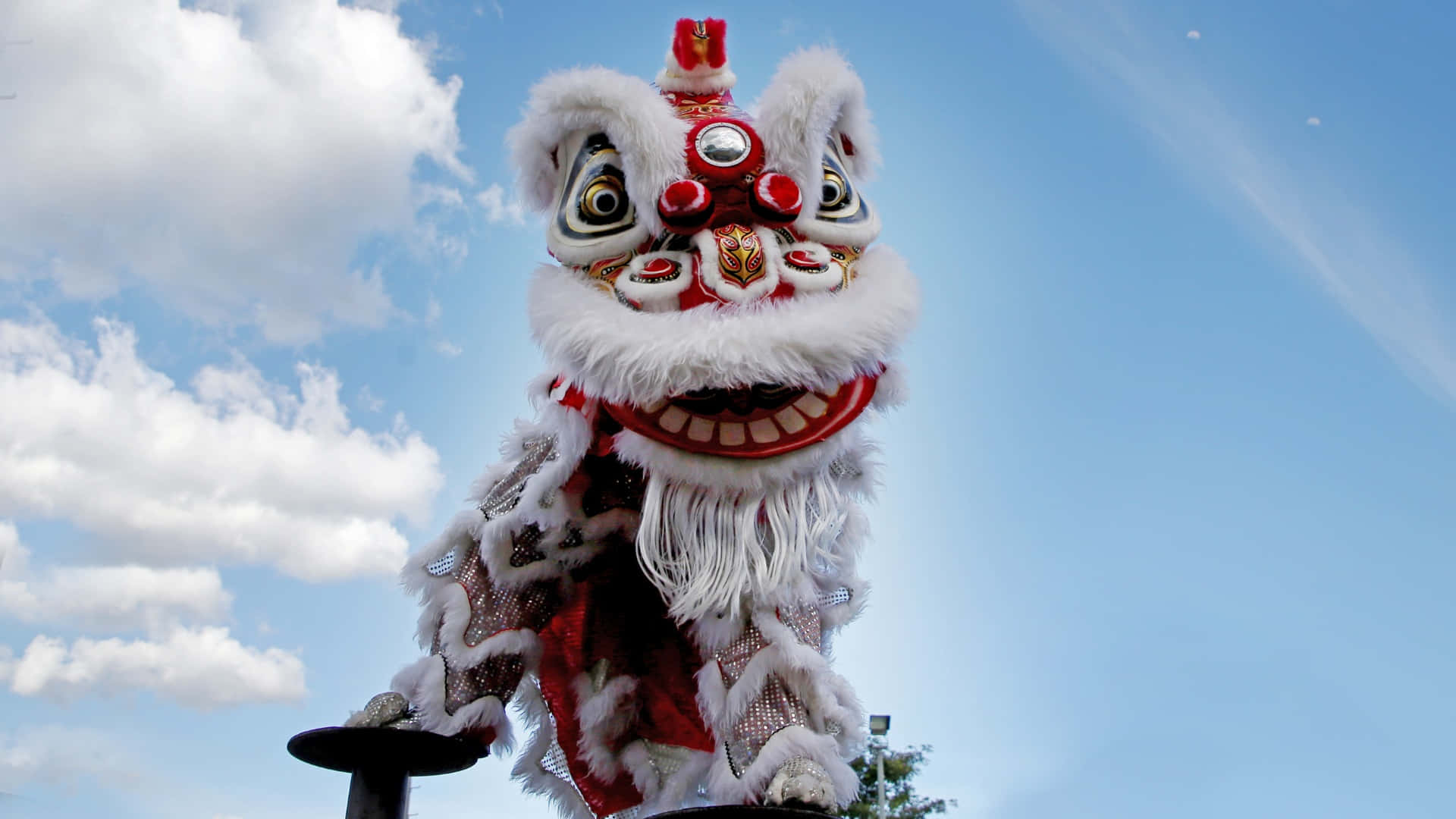  壁紙 — 一件鮮豔的白色和紅色中國舞獅服裝，在藍天白雲下高高聳立。