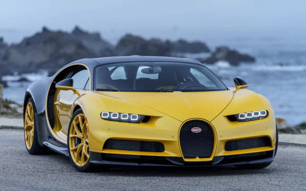 黃色Bugatti Chiron停泊在海邊道路上，背景有海浪和岩石。 — 4K 壁紙