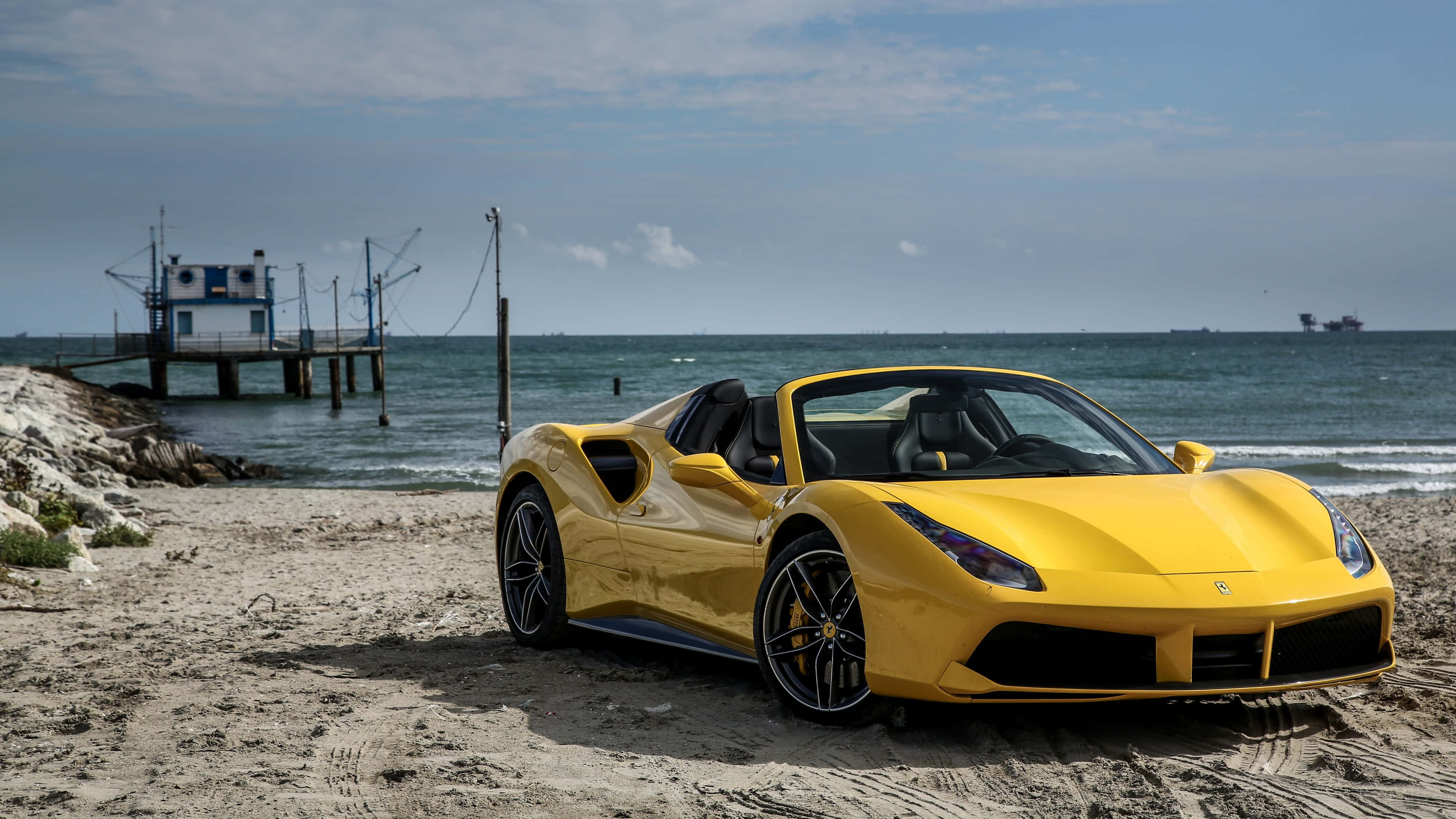Ferrari 488 Spider 桌布 壁紙 — 一輛鮮黃色的法拉利跑車停泊在沙灘上，背景有碼頭和海洋。