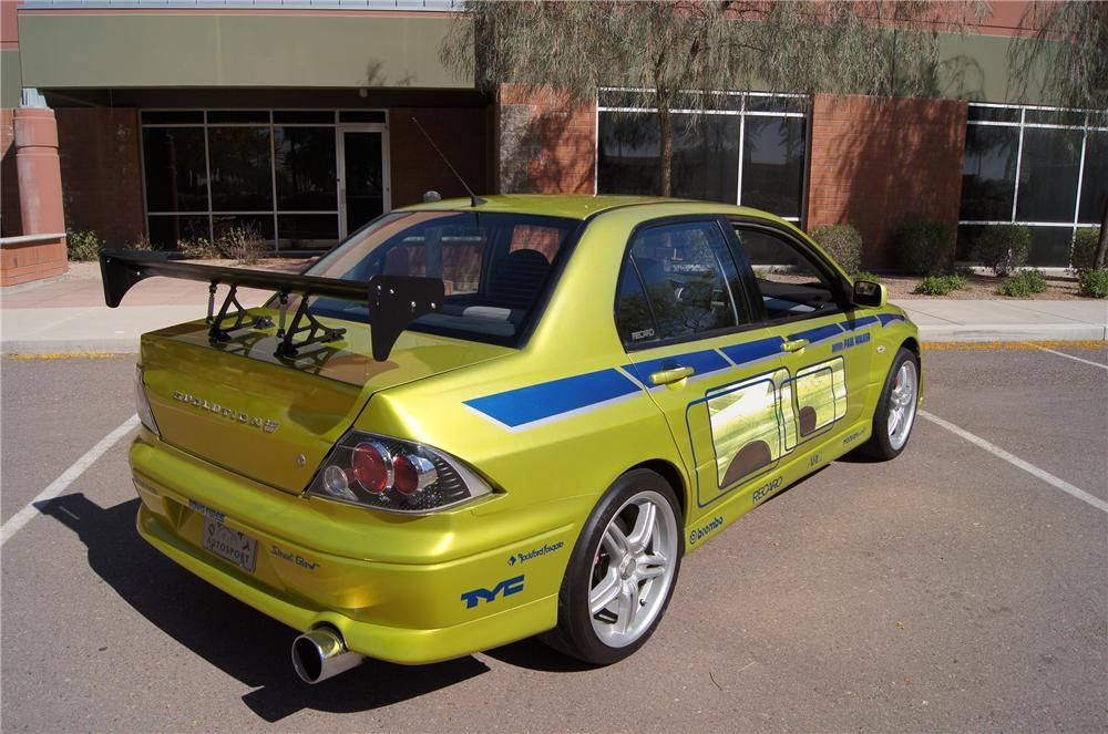 黃色三菱Lancer Evolution帶有賽車貼紙，停在陽光普照的停車場。 — 保羅·沃克汽車 壁紙