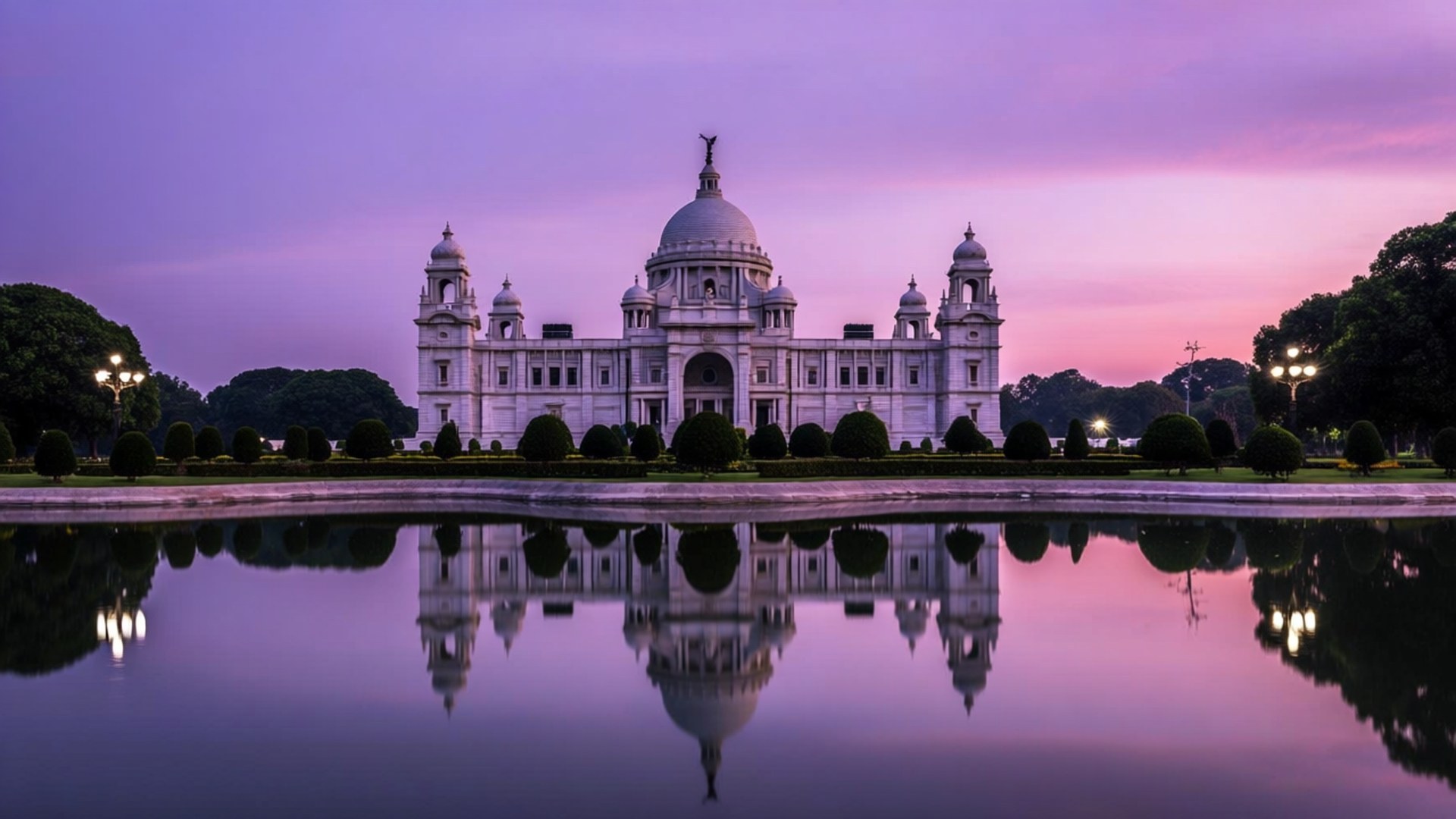 Victoria Memorial Dusk 壁紙 — 加爾各答的維多利亞紀念堂在紫粉色的暮色天空下閃耀著白光，完美地倒映在平靜的池塘中。