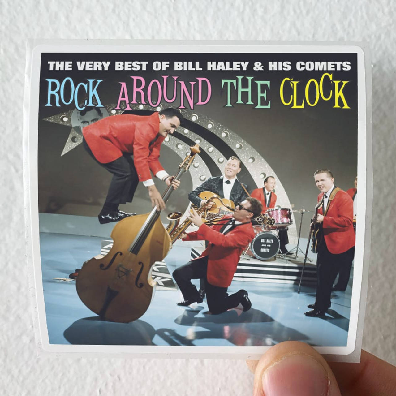 rock and roll 桌布 壁紙 — Bill Haley and His Comets 的復古專輯封面，他們穿著大膽的紅色西裝，以動態姿勢在星光時鐘背景下表演。