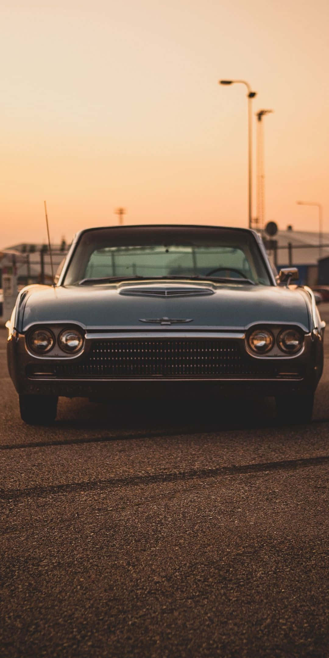 Ford Thunderbird 桌布 壁紙 — 一輛復古藍色敞篷跑車在溫暖的橙色日落天空下，面向前方停在柏油路上。