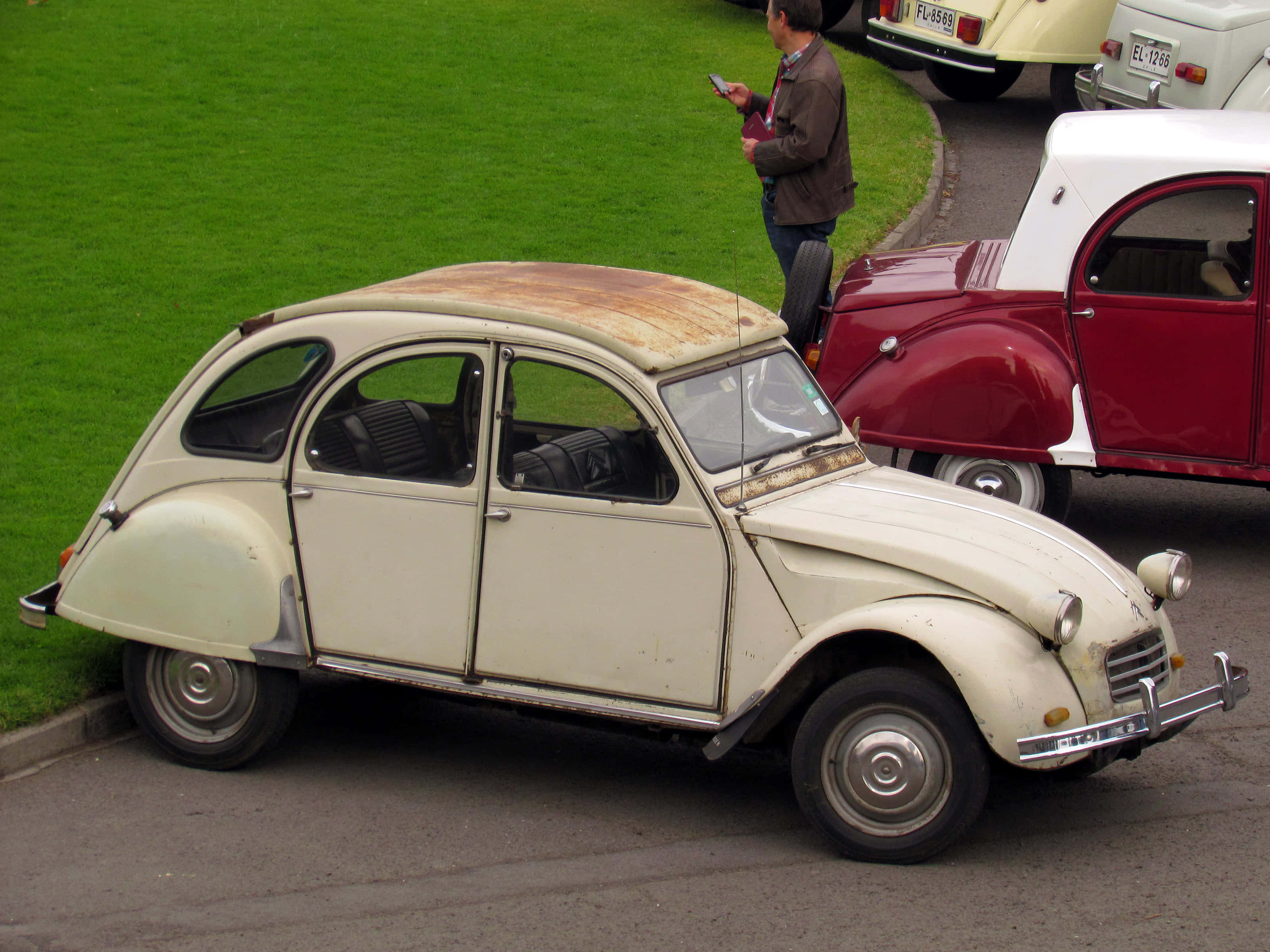 Citroen Ax 桌布 壁紙 — 一輛復古奶油色雪鐵龍2CV，帶有生鏽車頂，停泊在街上，旁邊有一輛紅白經典汽車。