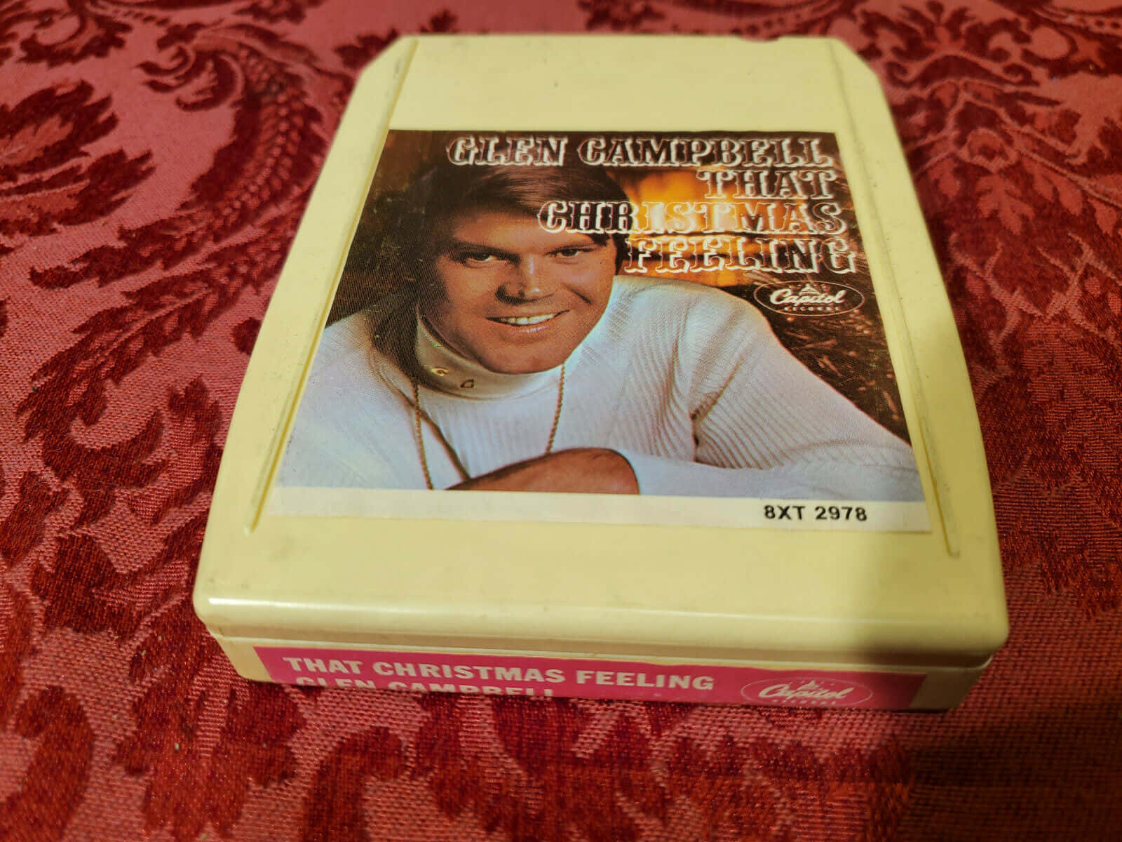  壁紙 — 一張復古的 Glen Campbell 聖誕卡式錄音帶放在豐富的紅色錦緞布料背景上。