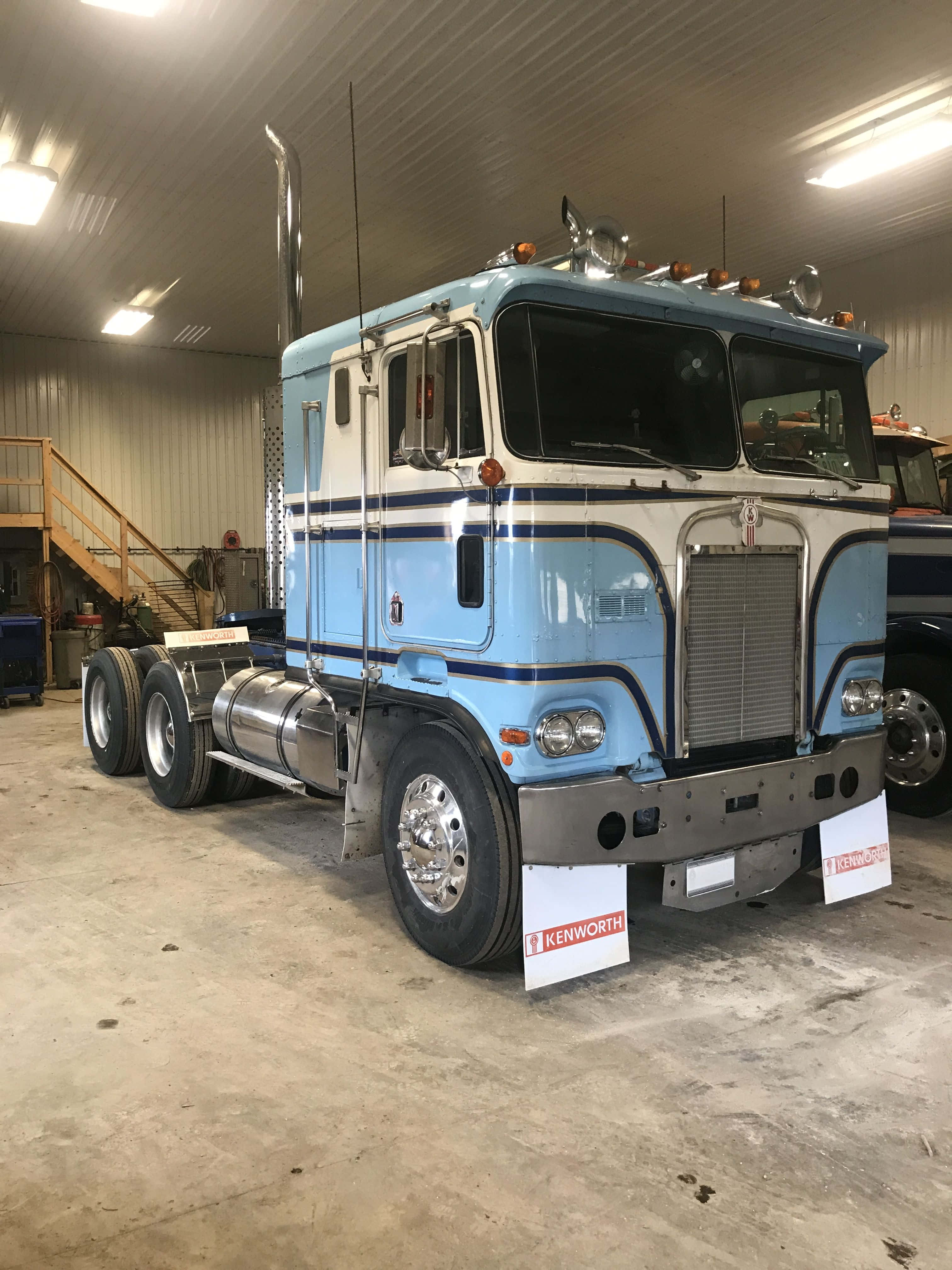 Kenworth K100 桌布 壁紙 — 一輛復古淺藍色和白色的 Kenworth 半掛卡車，帶有鍍鉻裝飾，停放在光線充足的金屬車庫內。