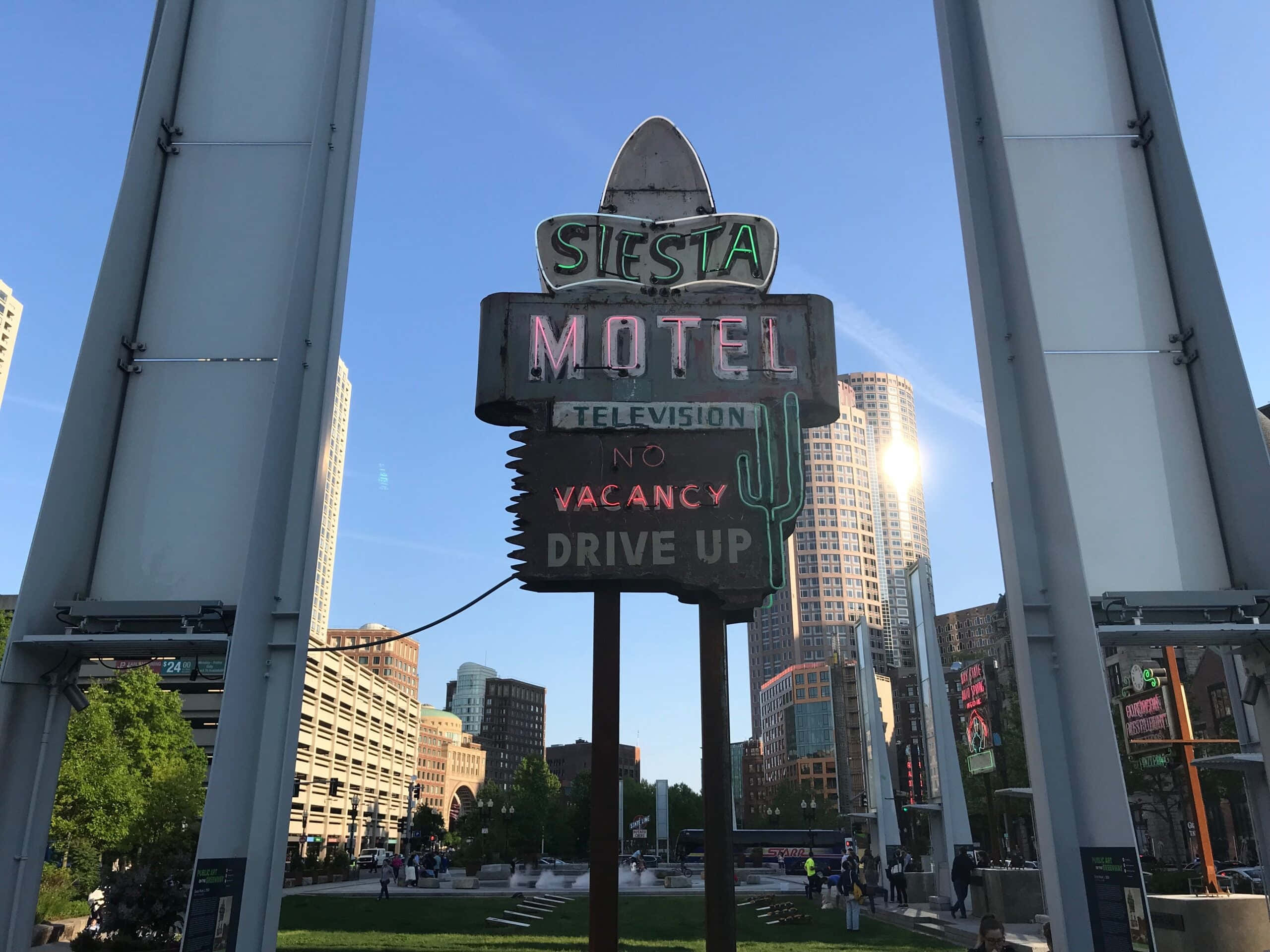Vintage Neon 桌布 壁紙 — 一個寫著「No Vacancy」的Siesta Motel復古霓虹招牌，矗立在晴朗藍天下的現代城市廣場上。