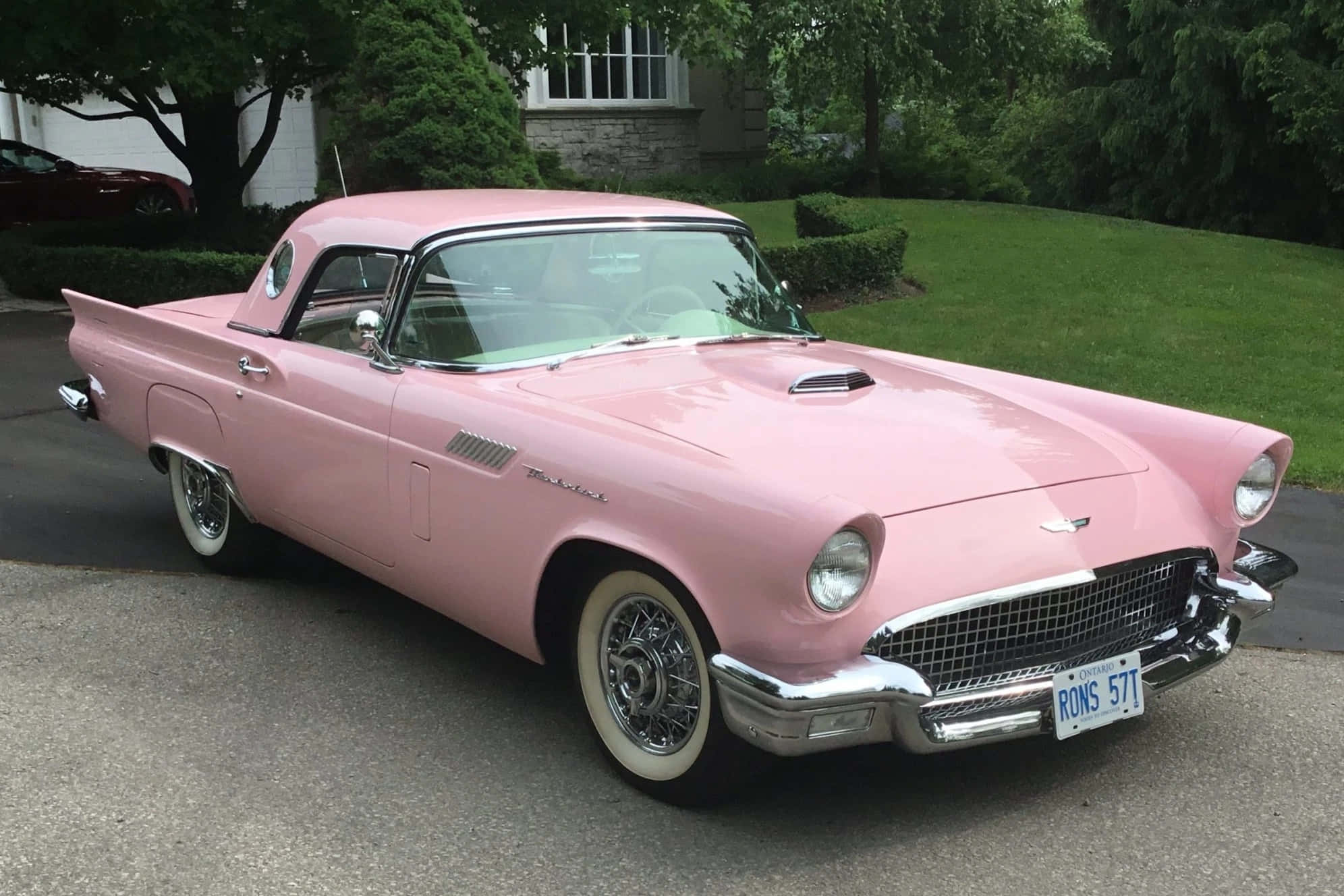 Ford Thunderbird 桌布 壁紙 — 一輛復古粉紅色福特雷鳥敞篷車停在車道上，背景有茂密的綠樹和石屋。