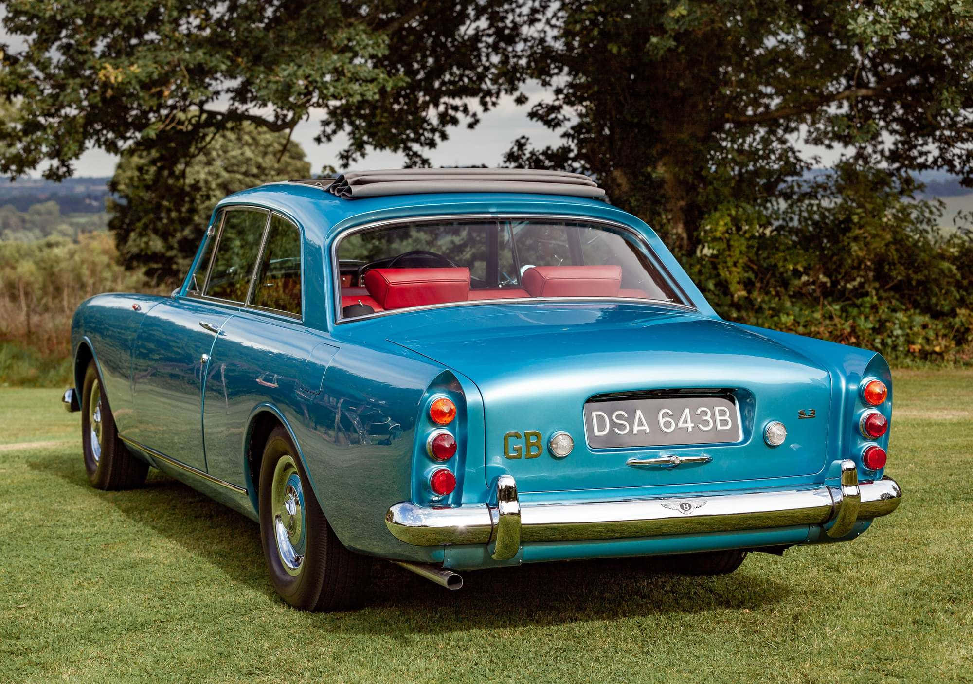 Bentley S3 桌布 壁紙 — 一輛復古青綠色Bentley S3，紅色內裝，停在樹葉茂密的樹下的草地上。