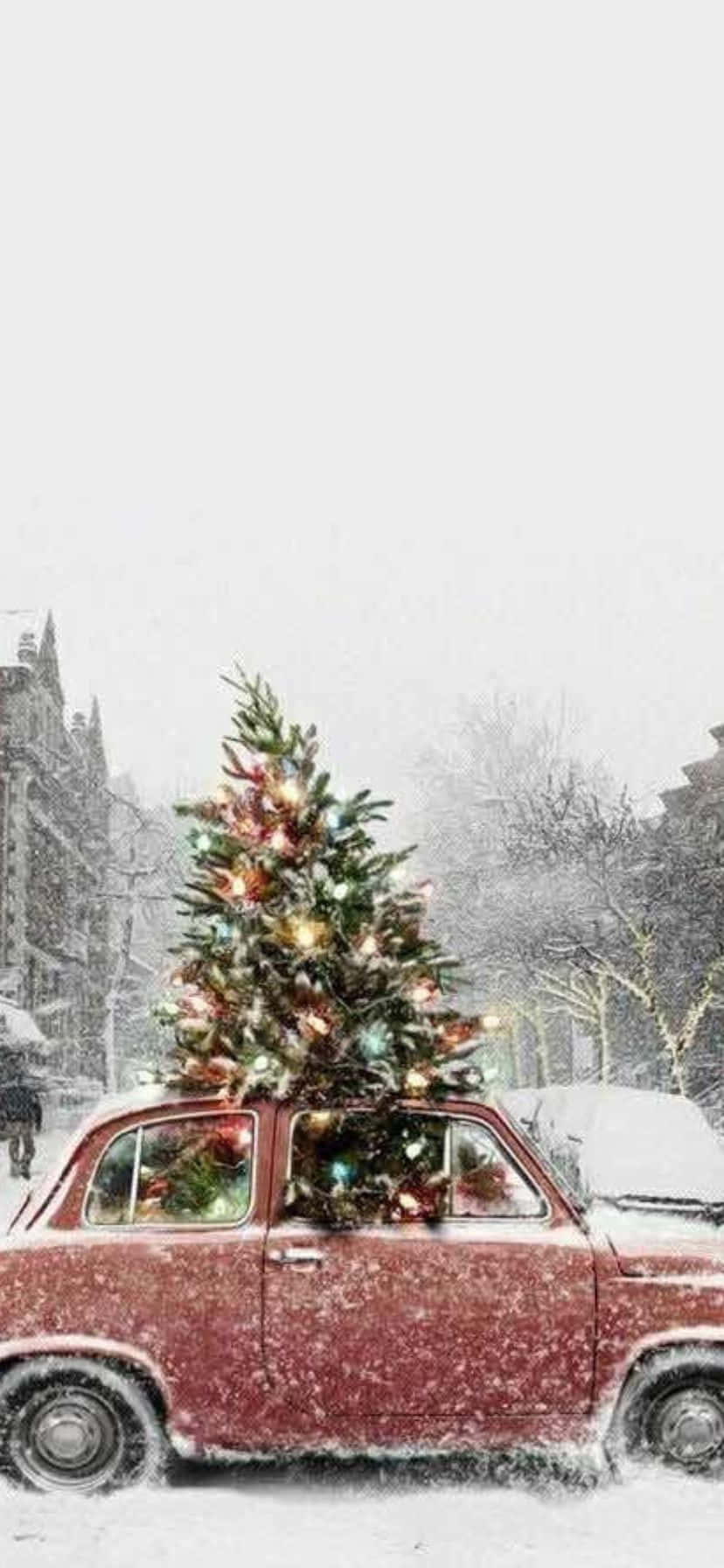  壁紙 — 一輛復古紅色汽車在積雪的街道上行駛，車頂載著一棵明亮裝飾的聖誕樹。
