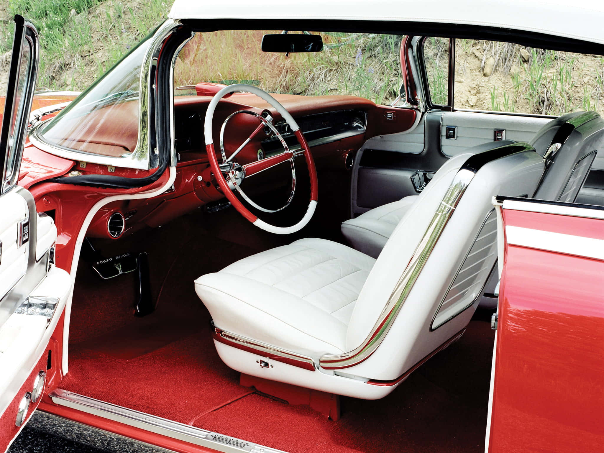 Cadillac Eldorado 桌布 壁紙 — 從打開的駕駛座車門看到的復古紅色汽車內部，配有白色皮革座椅和鍍鉻裝飾。