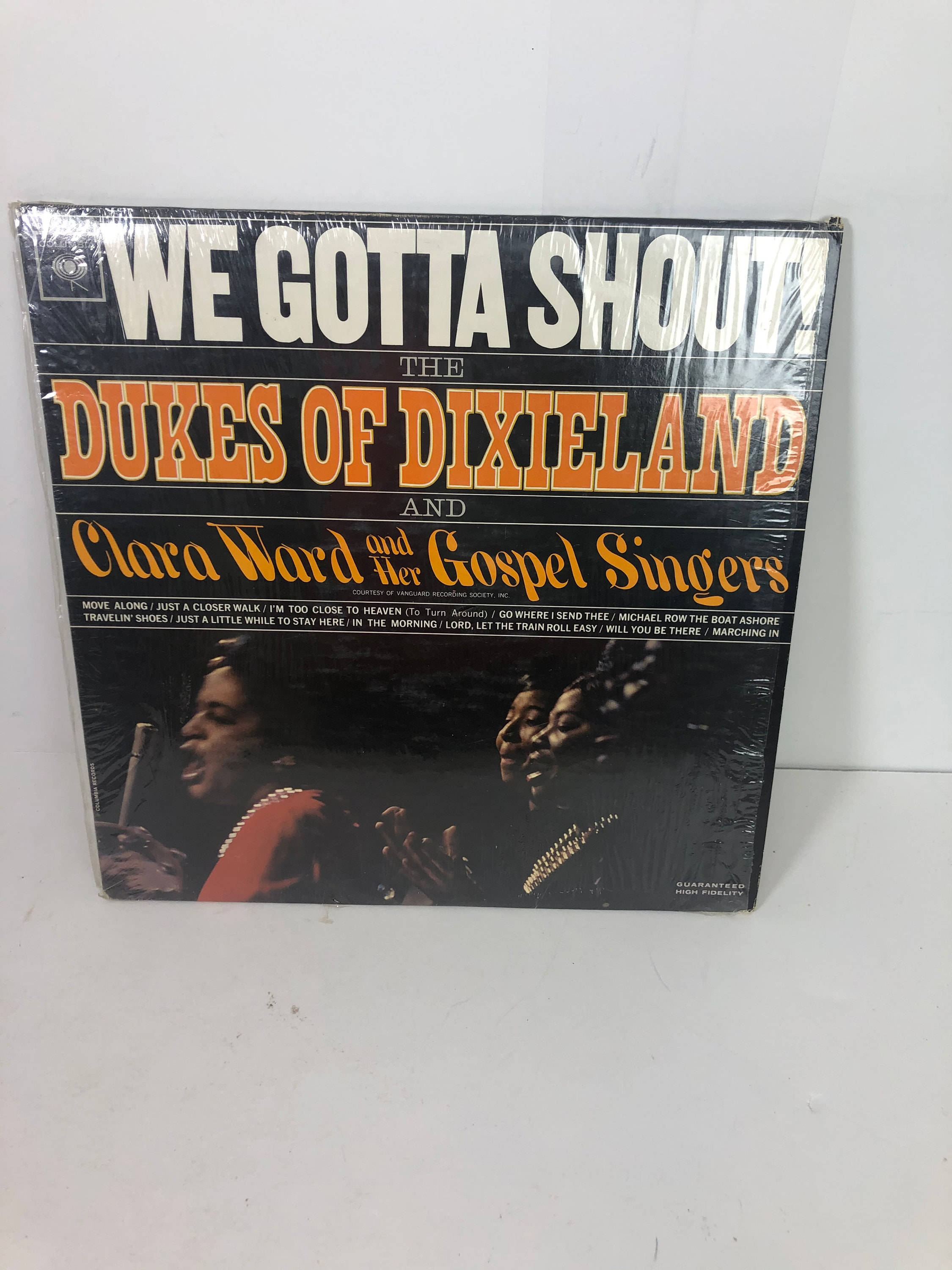 song 桌布 壁紙 — The Dukes of Dixieland 和 Clara Ward and Her Gospel Singers 的《We Gotta Shout》復古黑膠唱片專輯封面，密封在塑膠中，展示在純白色背景上。
