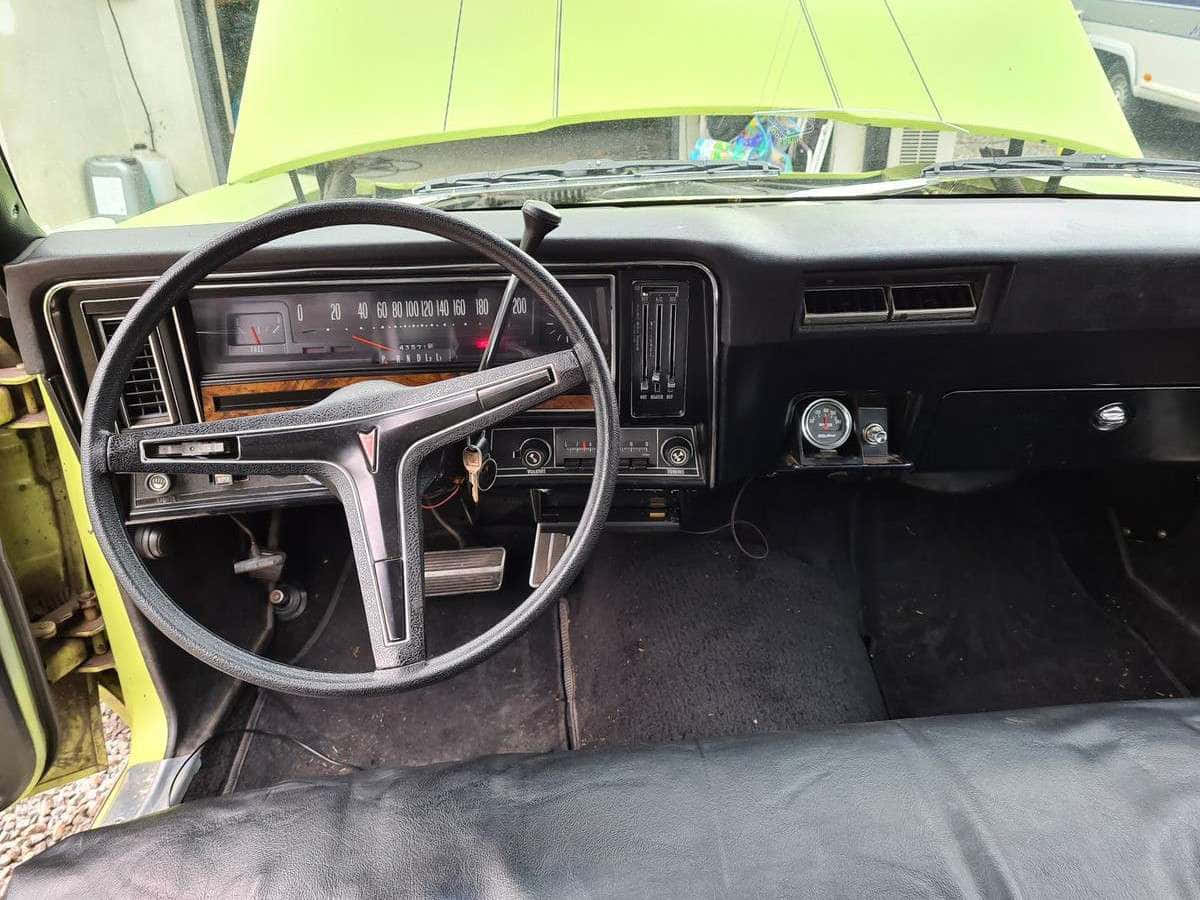 Pontiac Ventura 桌布 壁紙 — 充滿活力的青檸綠色經典汽車內飾，配備黑色儀表板和方向盤，展現70年代復古設計和磨損的黑色皮革座椅。