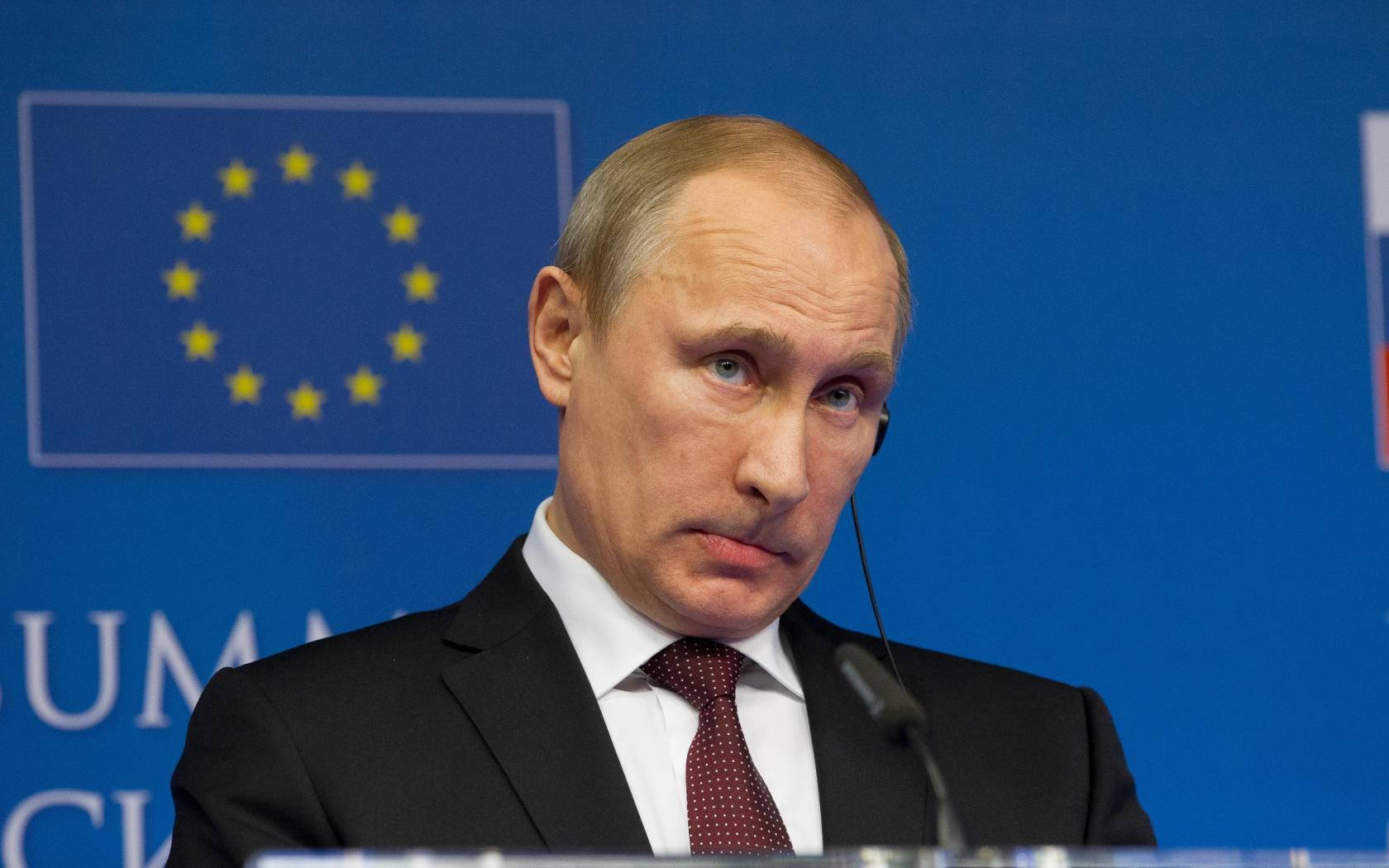 Leadership 桌布 壁紙 — Vladimir Putin 身穿深色西裝和紅色領帶，在背後有藍色歐盟旗幟的講台上發言。