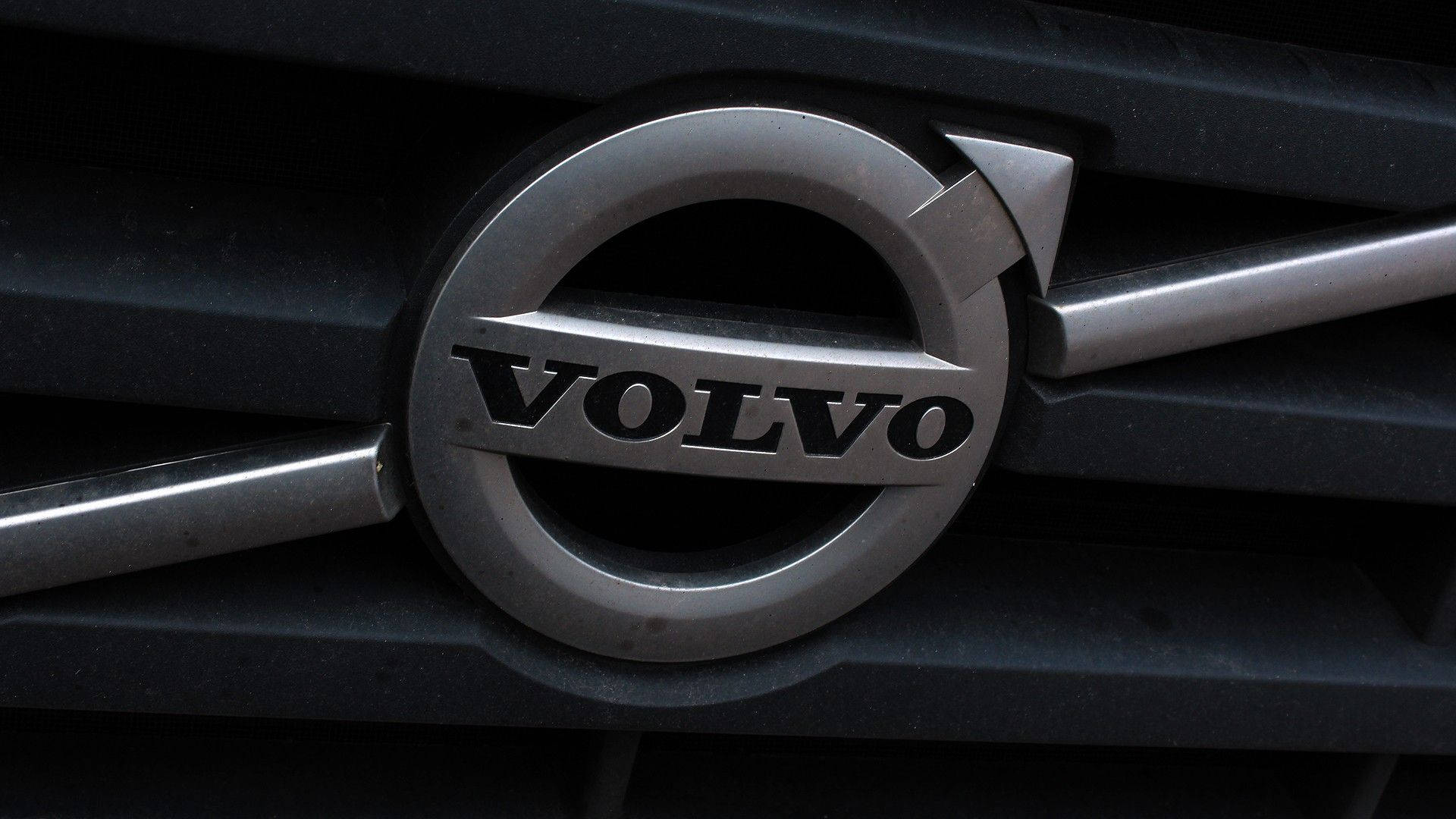 Volvo 桌布 壁紙 — Volvo 汽車標誌在深色格柵上的特寫，帶有金屬光澤和銳利照明。