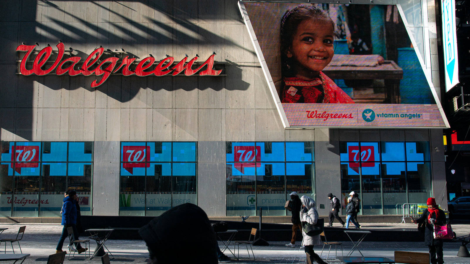 商業 桌布 壁紙 — Walgreens 商店外牆，有一個微笑小孩的大型廣告牌，白天有行人走過。
