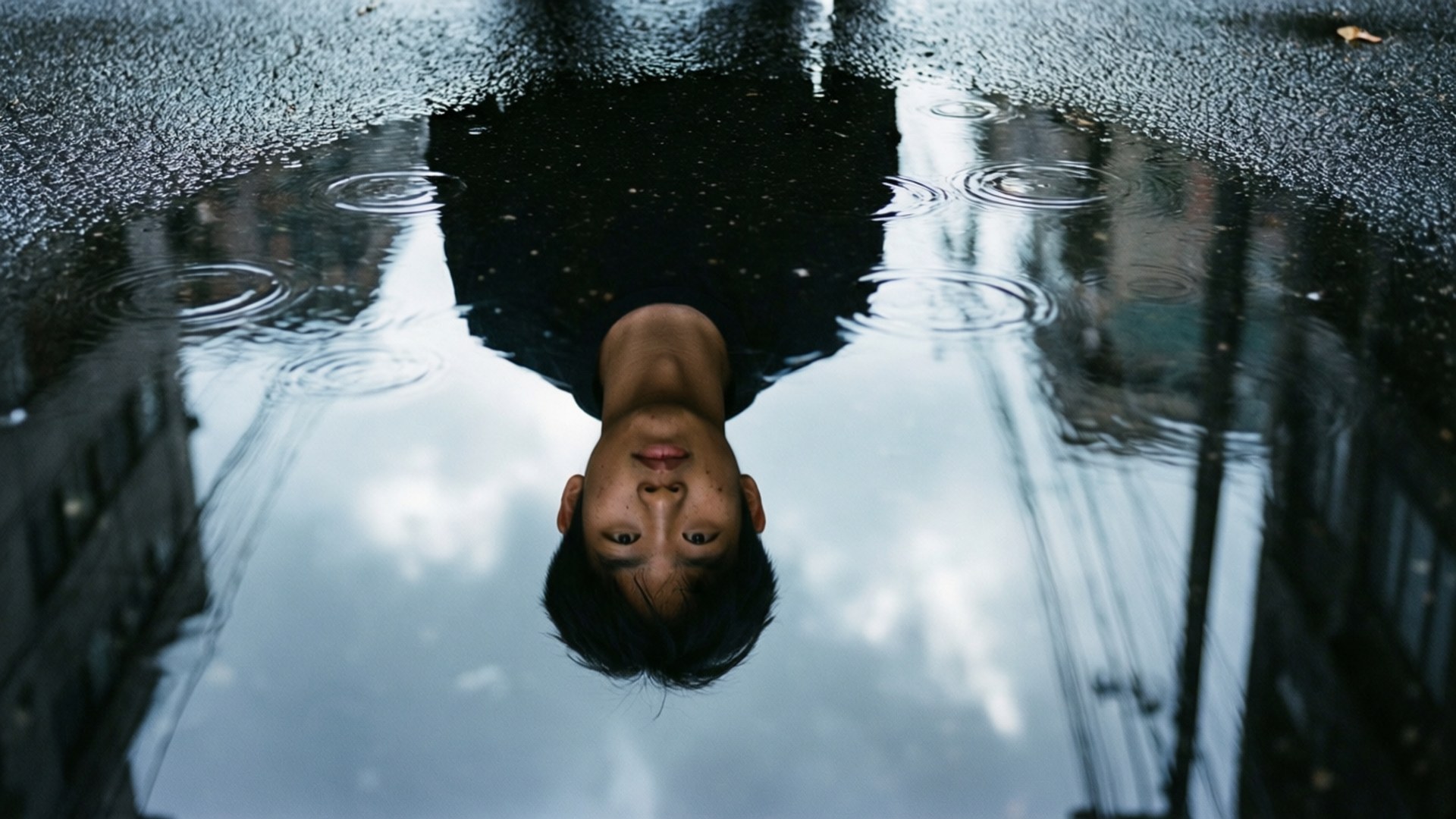 Tayo 桌布 壁紙 — 一個年輕男子在雨水濕滑的城市水坑中的倒影，因落下的水滴而泛起漣漪。