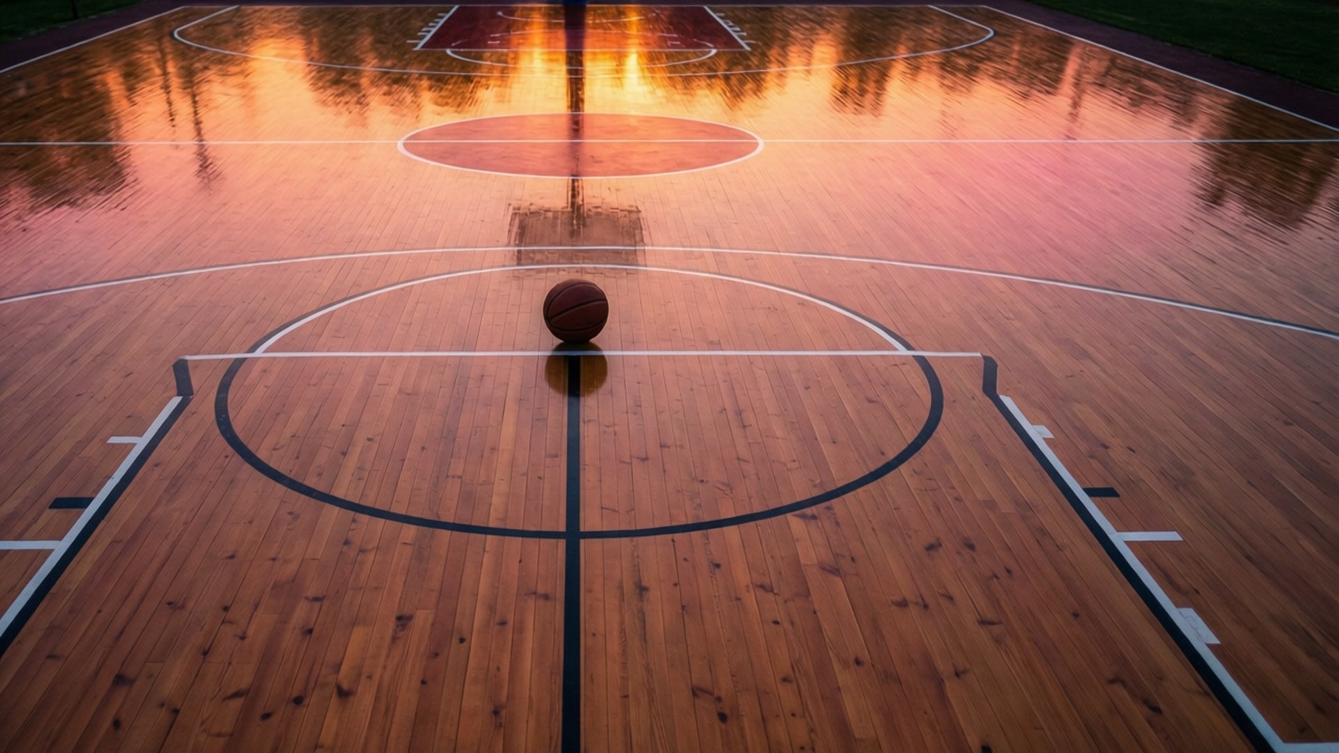 Sunset at Center Court 壁紙 — 一個籃球放在球場中央的拋光木地板上，沐浴在溫暖的日落倒影中。