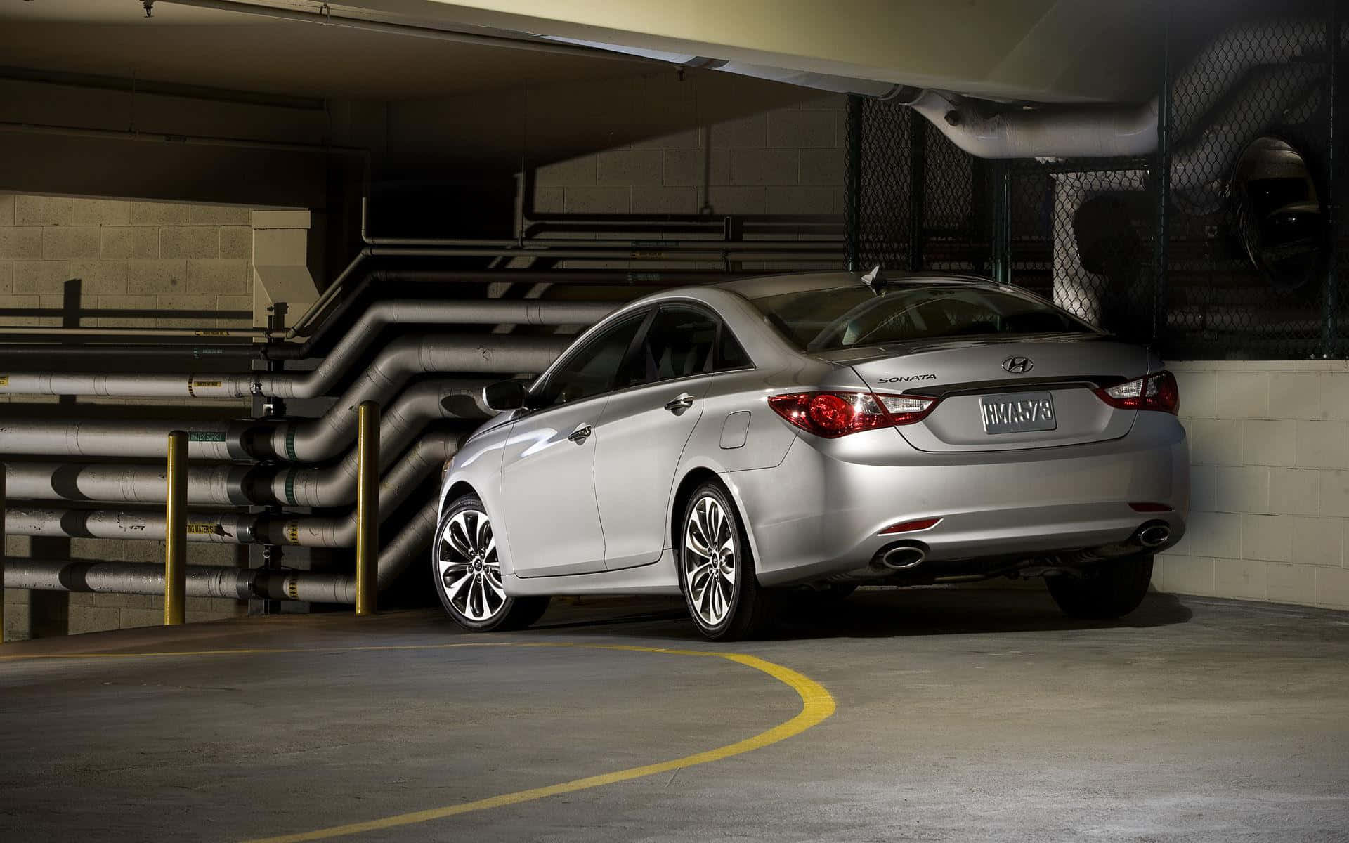 Hyundai Sonata 桌布 壁紙 — 一輛時尚的銀色轎車停放在光線昏暗的地下停車場，內有工業管道和黃色標線。