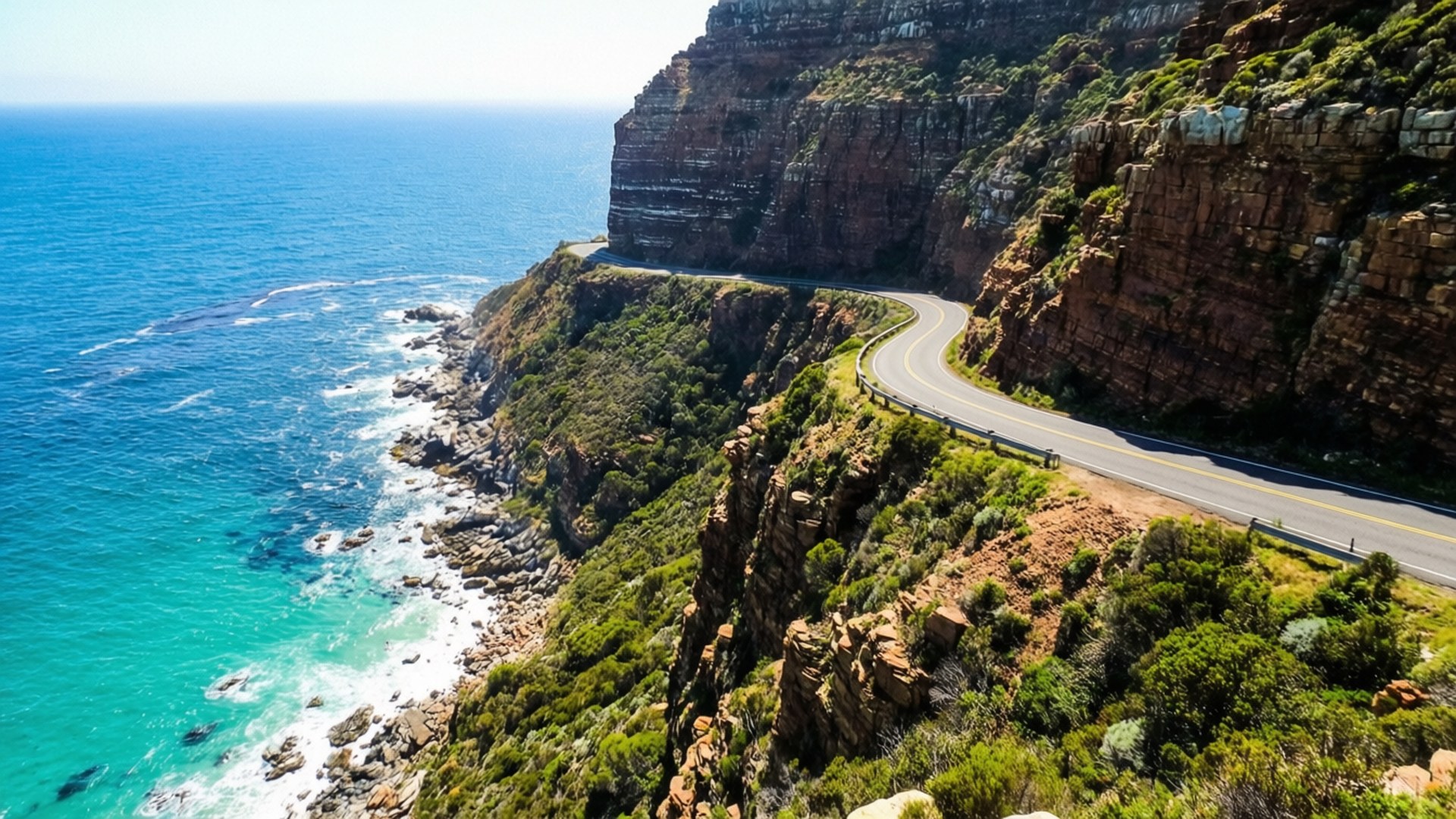 Chapman's Peak Drive 壁紙 — 一條蜿蜒的海岸公路緊貼著崎嶇的懸崖，俯瞰著碧綠的海浪拍打岩石海岸。