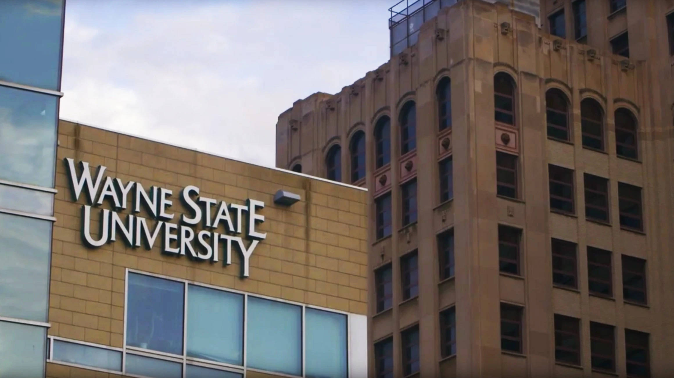 Building 桌布 壁紙 — Wayne State University 建築物，擁有現代玻璃外牆和經典石塔，在陰天天空下。