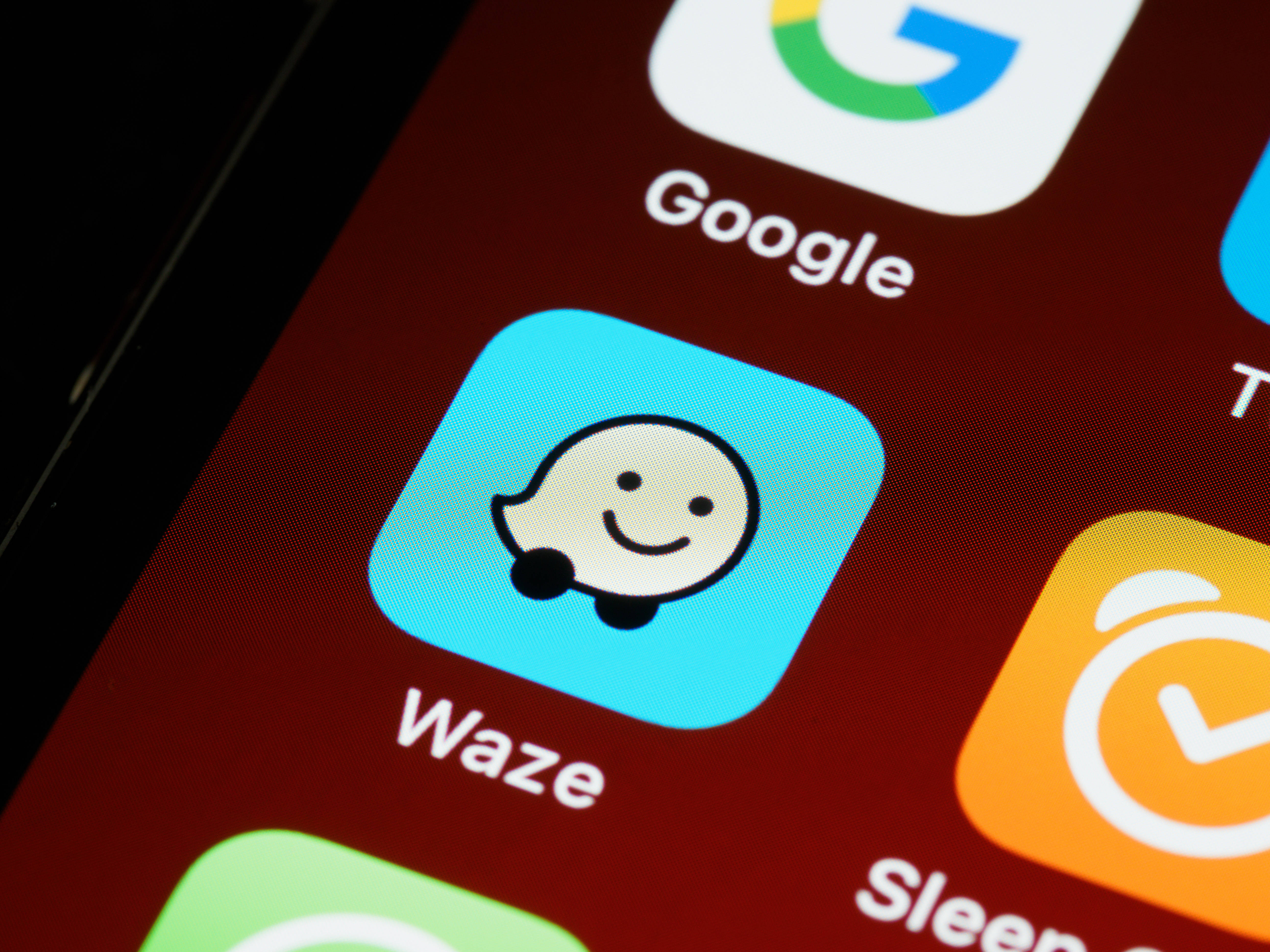 Waze應用 iOS 13 壁紙 — 智慧型手機螢幕特寫，顯示Waze應用程式圖標，帶有微笑鬼魂吉祥物，背景為藍色。