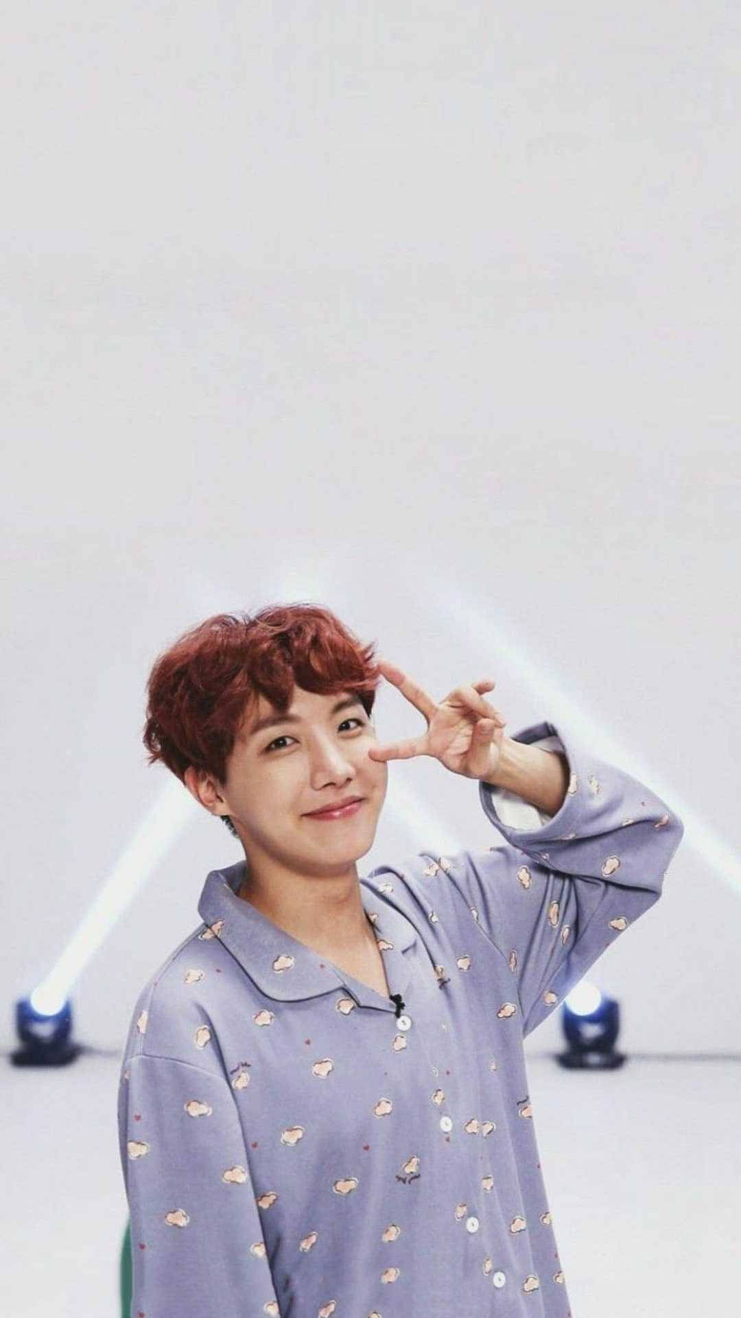 紅髮年輕男子在工作室中微笑並比出和平手勢，背景有聚光燈。 — Bts 壁紙