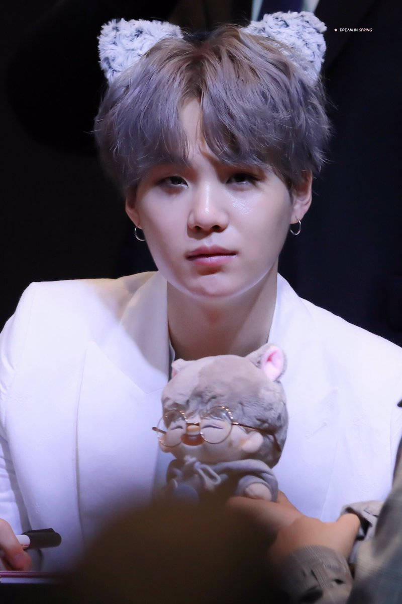 年輕男子穿白色西裝在粉絲活動中抱著戴眼鏡的毛絨貓。 — Bts 壁紙