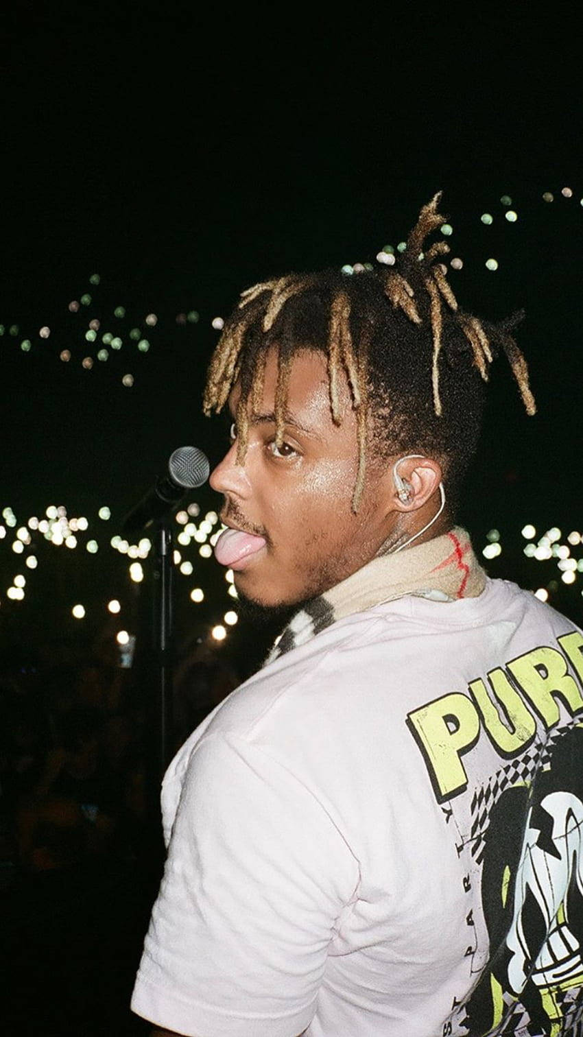 年輕男子在夜晚舞台上伸出舌頭表演，身後有串燈。 — Juice Wrld 壁紙