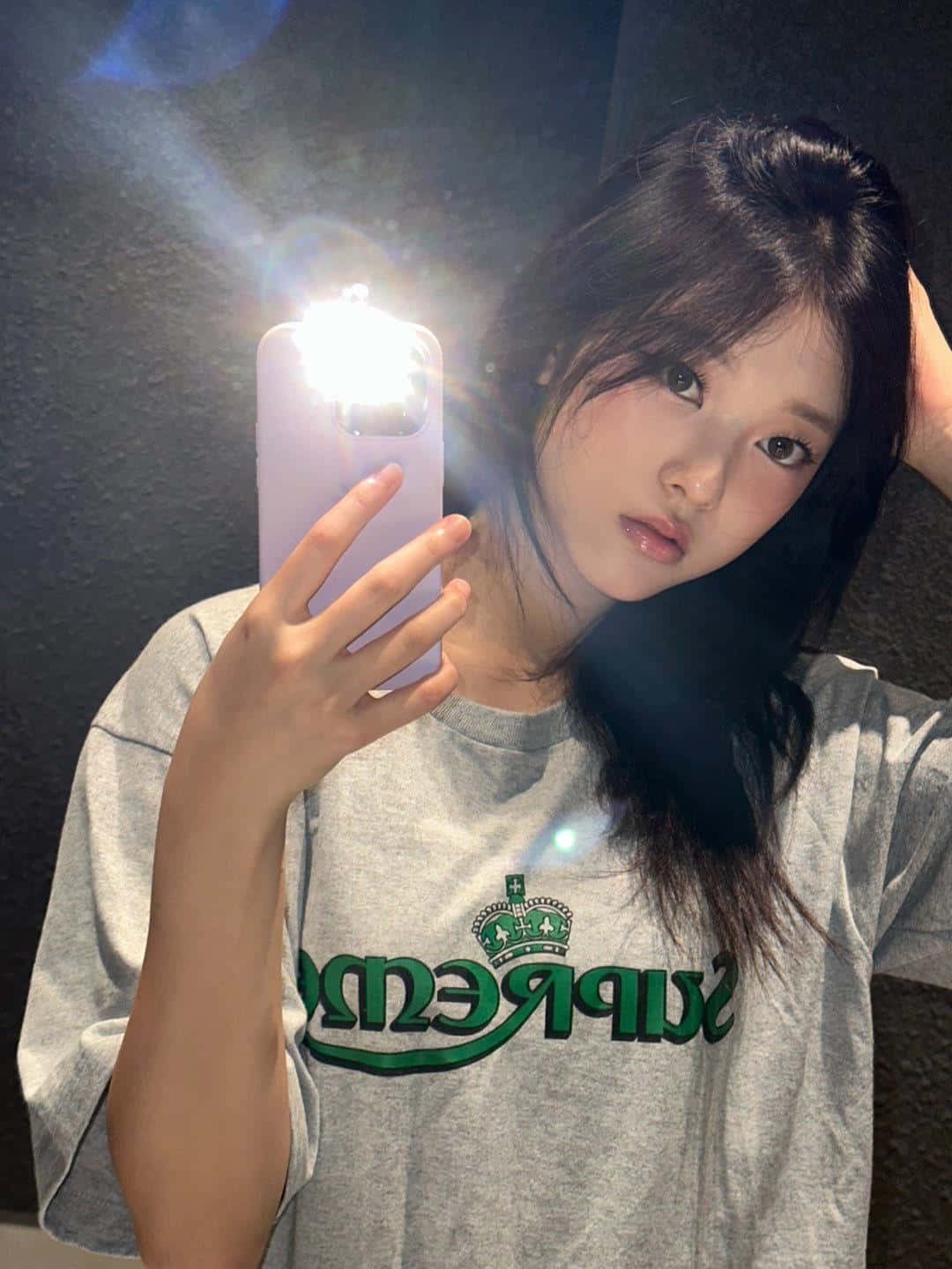  壁紙 — 一位深色頭髮的年輕女性在昏暗的房間裡拿著發光的手機對著鏡子自拍。