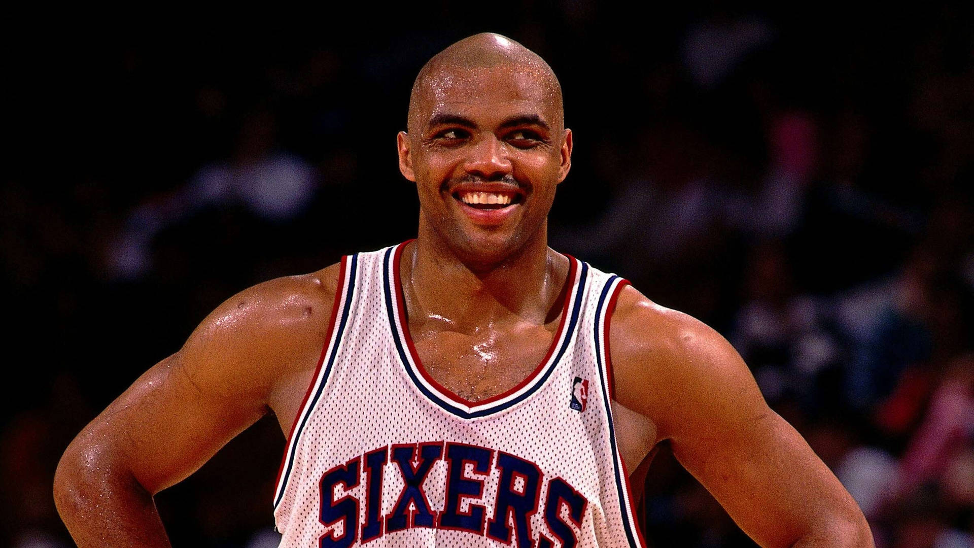 身穿Sixers球衣的籃球運動員微笑雙手叉腰。 — NBA 壁紙