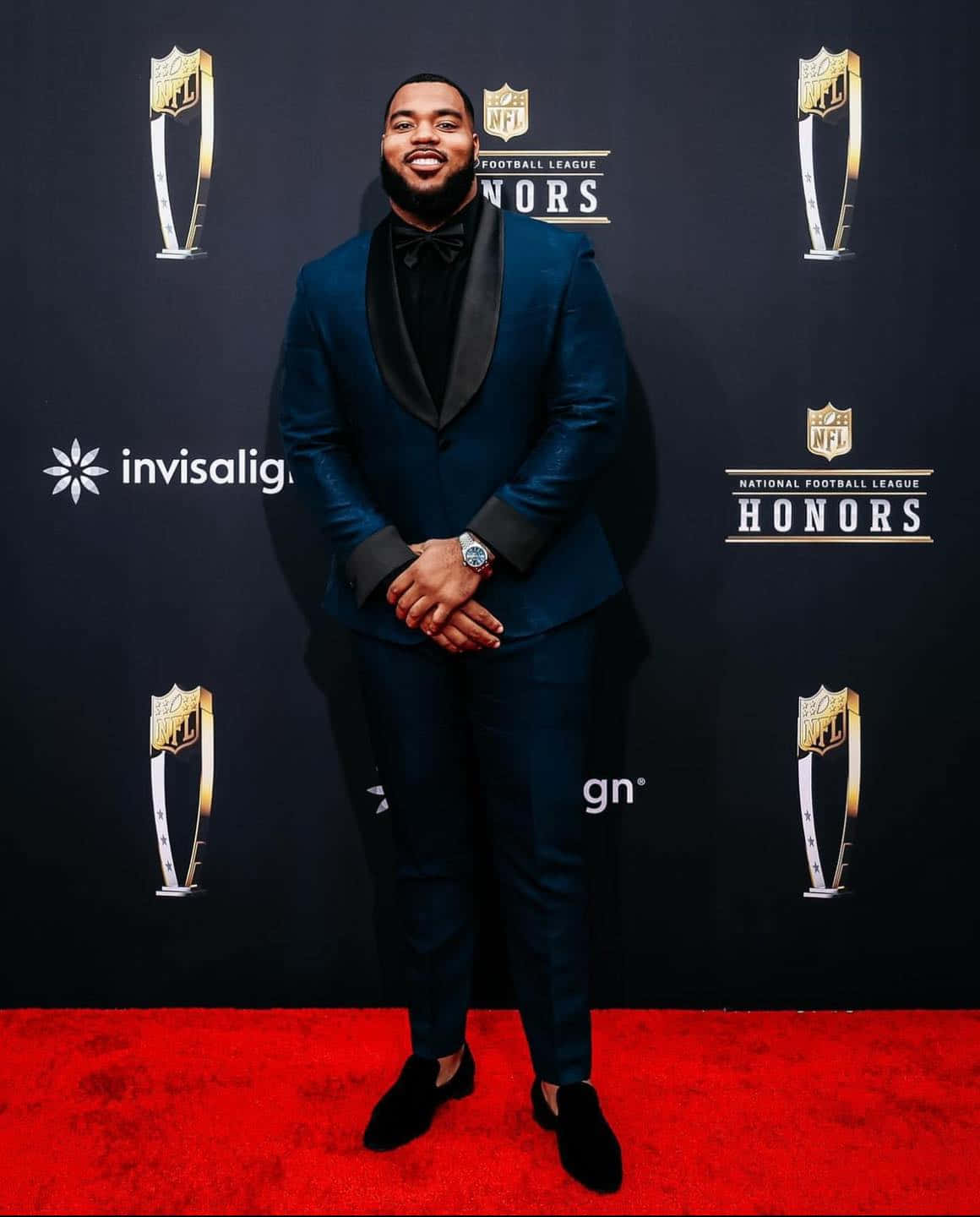  壁紙 — 一位微笑的男子身穿藍色燕尾服，自信地站在NFL Honors活動的紅地毯上，身後有標誌。