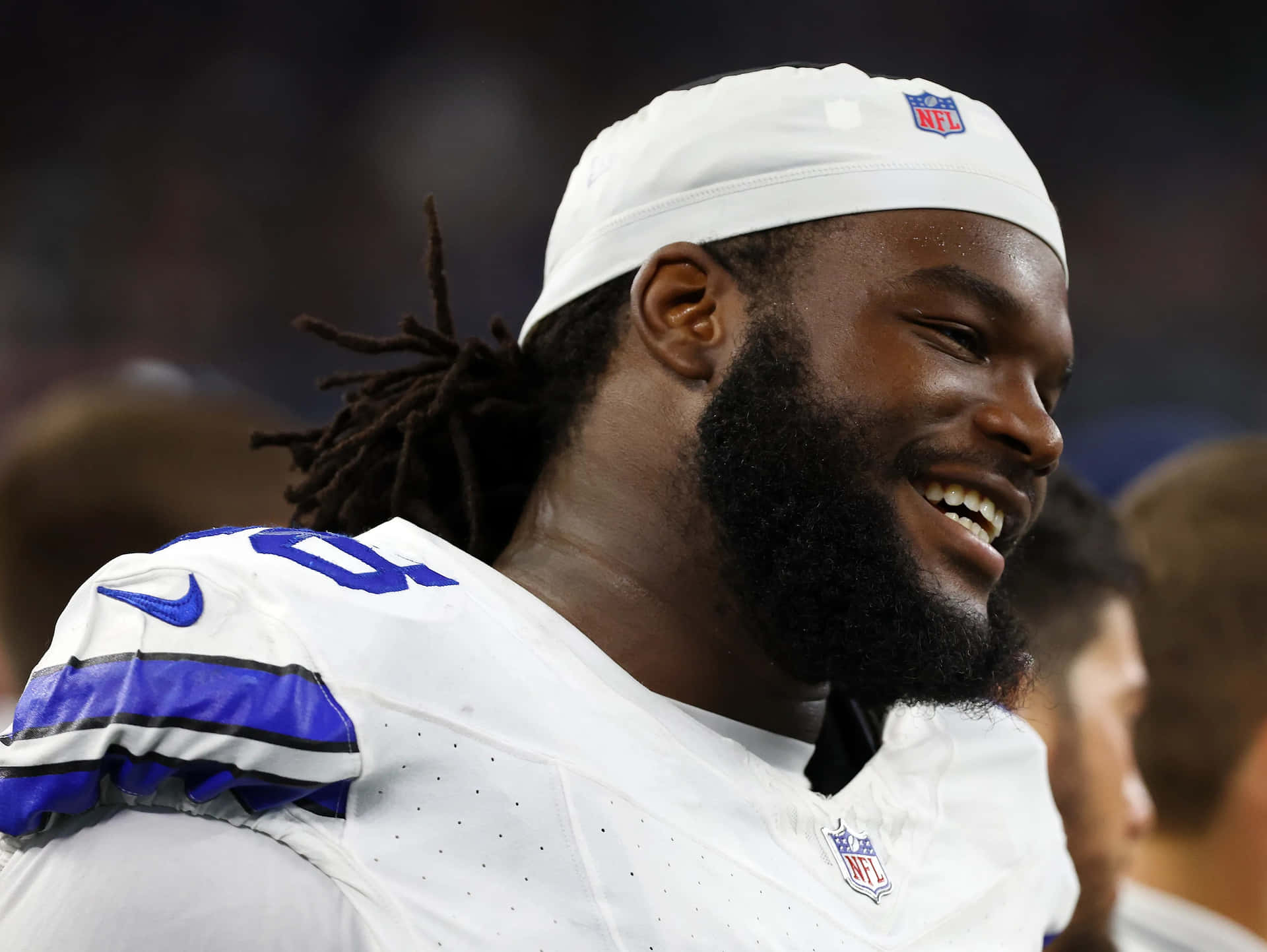  壁紙 — 一位微笑的NFL美式足球員，身穿白色球衣和頭帶，在球場燈光下比賽時大笑。