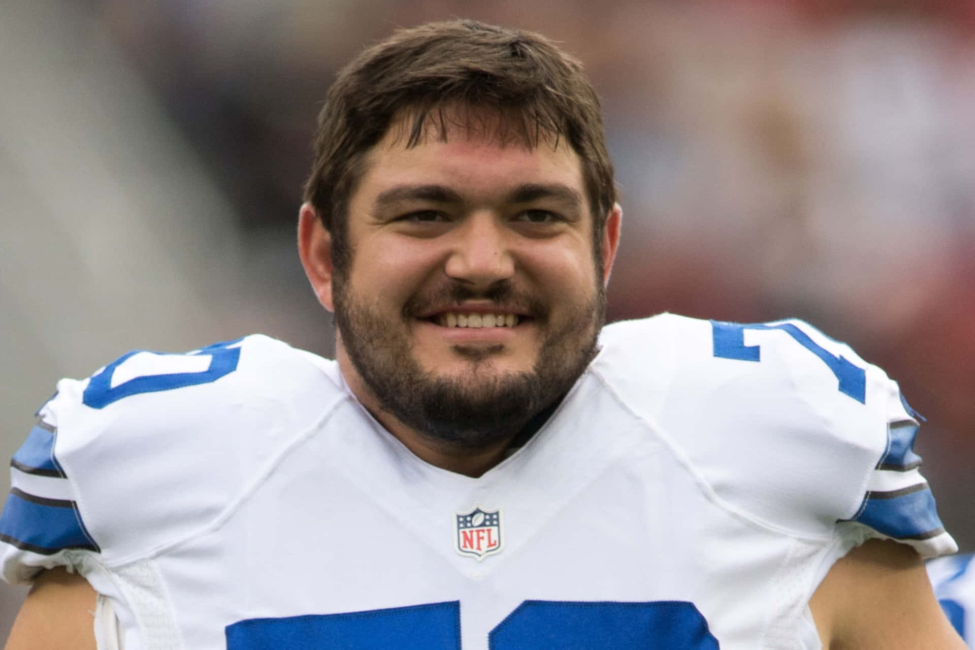  壁紙 — 一位微笑的NFL美式足球員，身穿白色和藍色球衣，肩上印有71號。