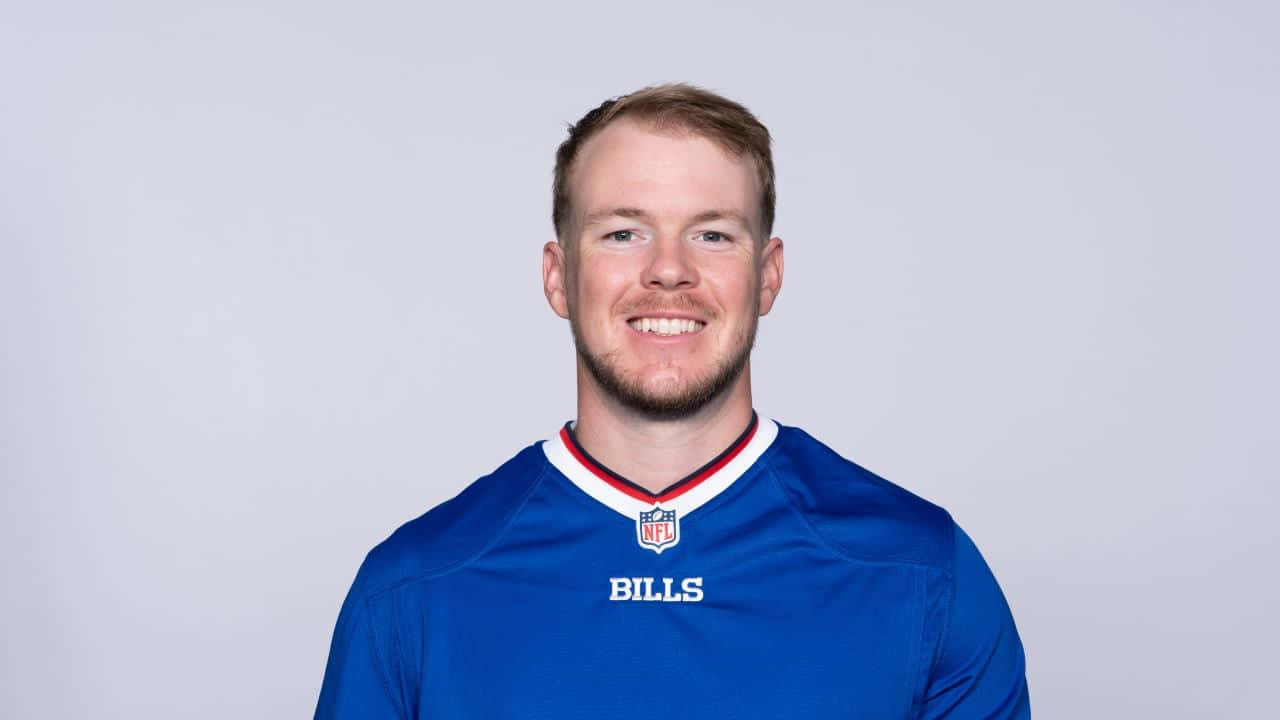  壁紙 — 一位微笑的男子身穿藍色水牛城比爾隊NFL球衣，在純淺灰色攝影棚背景前擺姿勢。