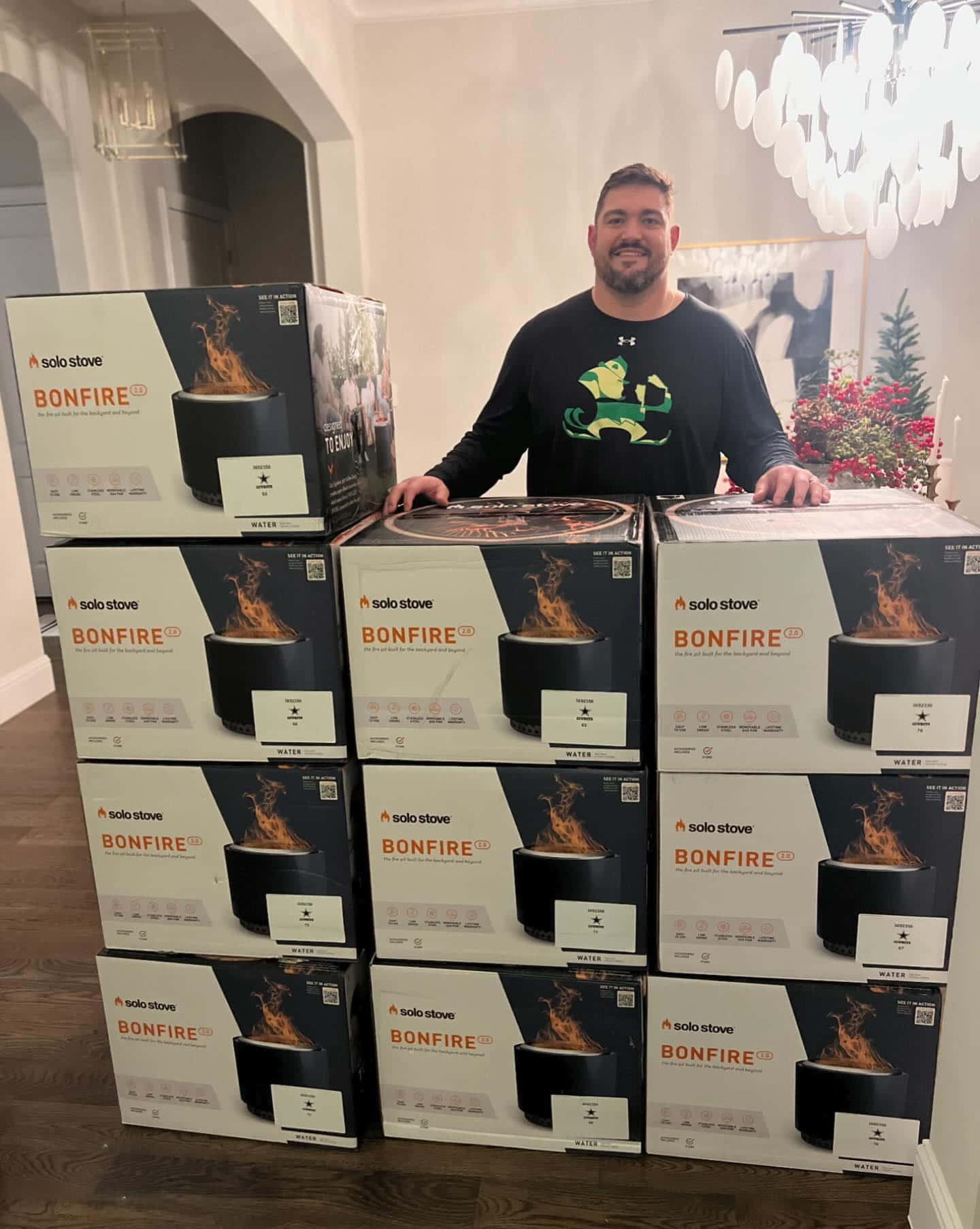  壁紙 — 一位微笑的男子自豪地站在現代家居室內的一大堆Solo Stove Bonfire產品盒後面。