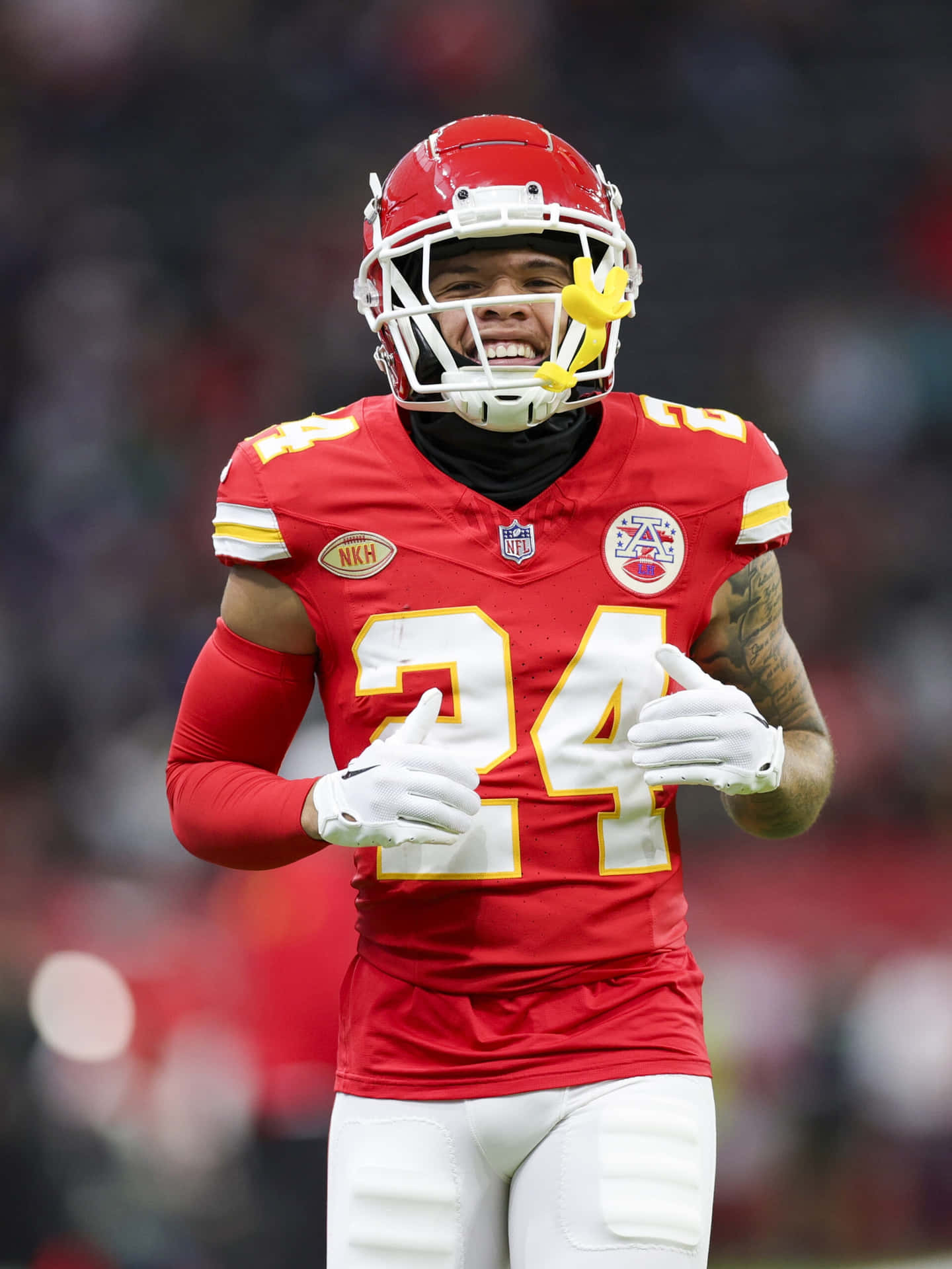  壁紙 — 一位微笑的NFL美式足球員身穿紅色24號球衣，戴著有黃色花朵的頭盔，豎起兩個大拇指。