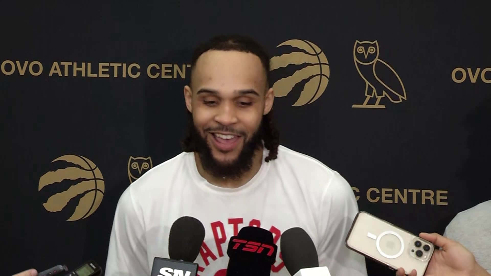 籃球運動員在記者會上微笑，面前有記者和手機。 — NBA 壁紙