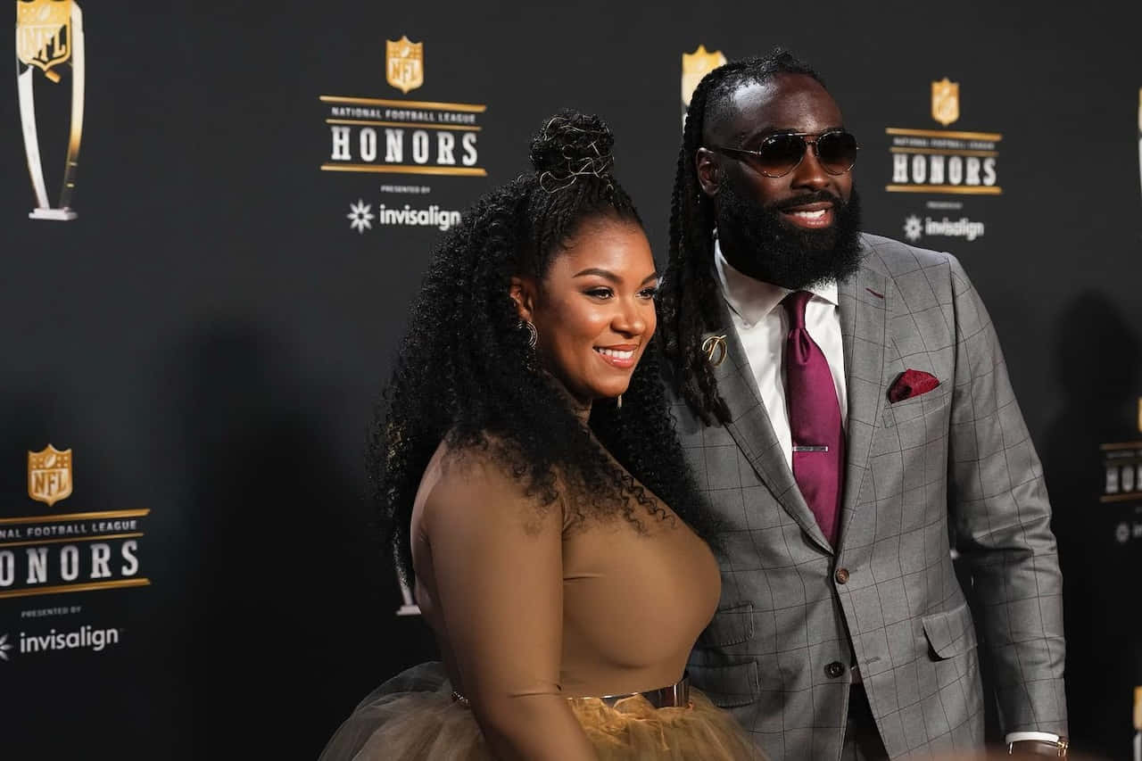  壁紙 — 一對微笑的情侶在印有NFL Honors標誌和贊助商品牌的黑色活動背景前擺姿勢。