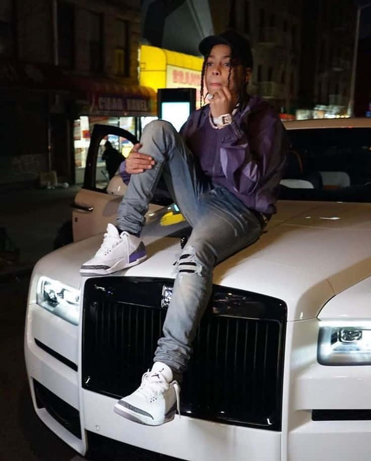  壁紙 — 一位紮辮的年輕人夜晚在城市街道上隨意坐在白色豪華車頂上，被霓虹燈和街燈照亮。