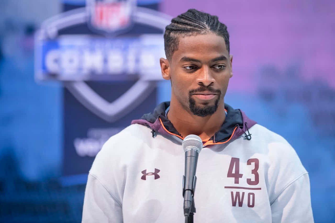  壁紙 — 一位專注的美式足球員身穿白色連帽衫，號碼43，站在NFL聯合測試活動的麥克風前。