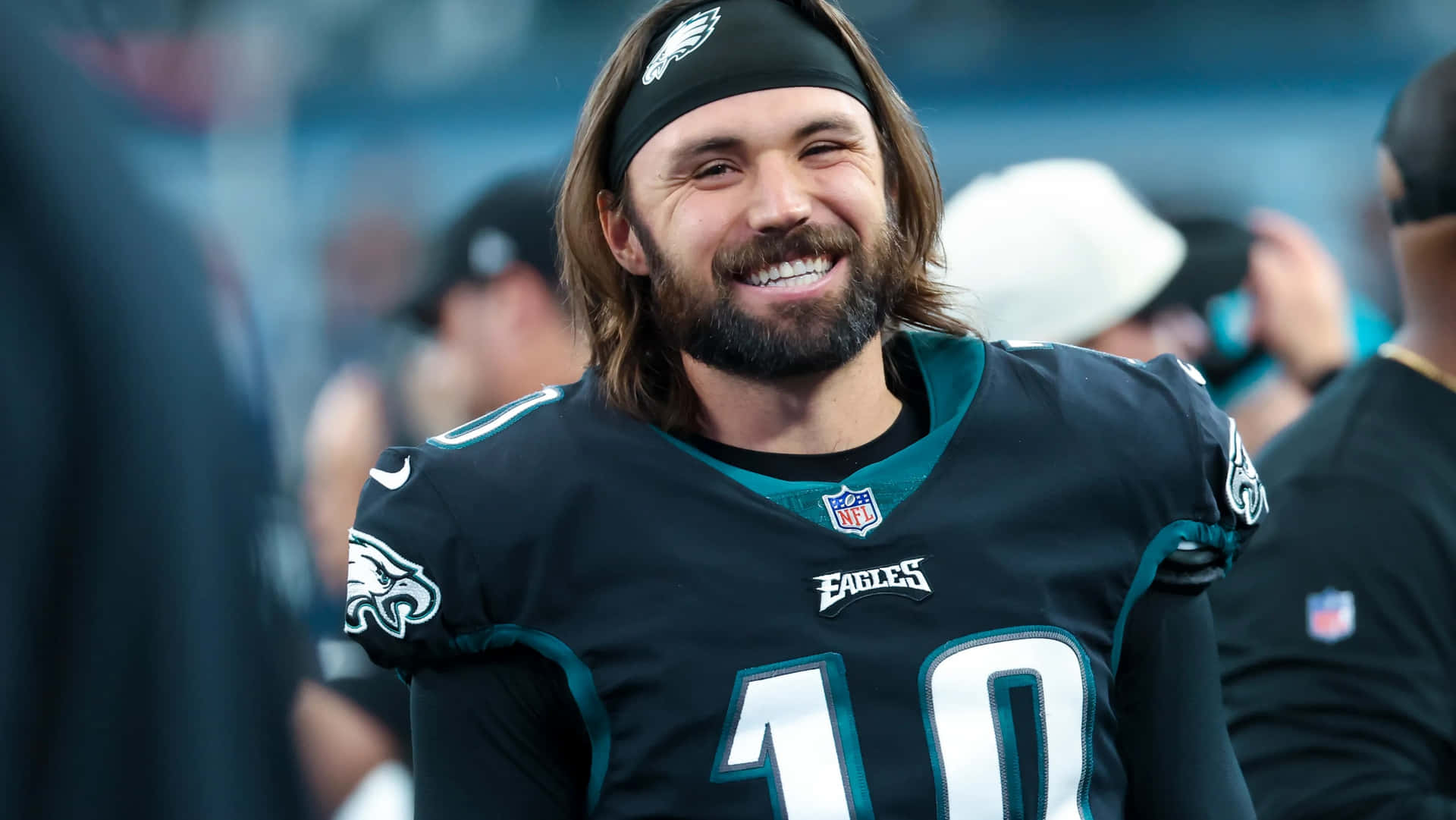  壁紙 — 一位微笑的美式足球員身穿黑色Eagles球衣，背號10號，在體育場上對著鏡頭綻放笑容。
