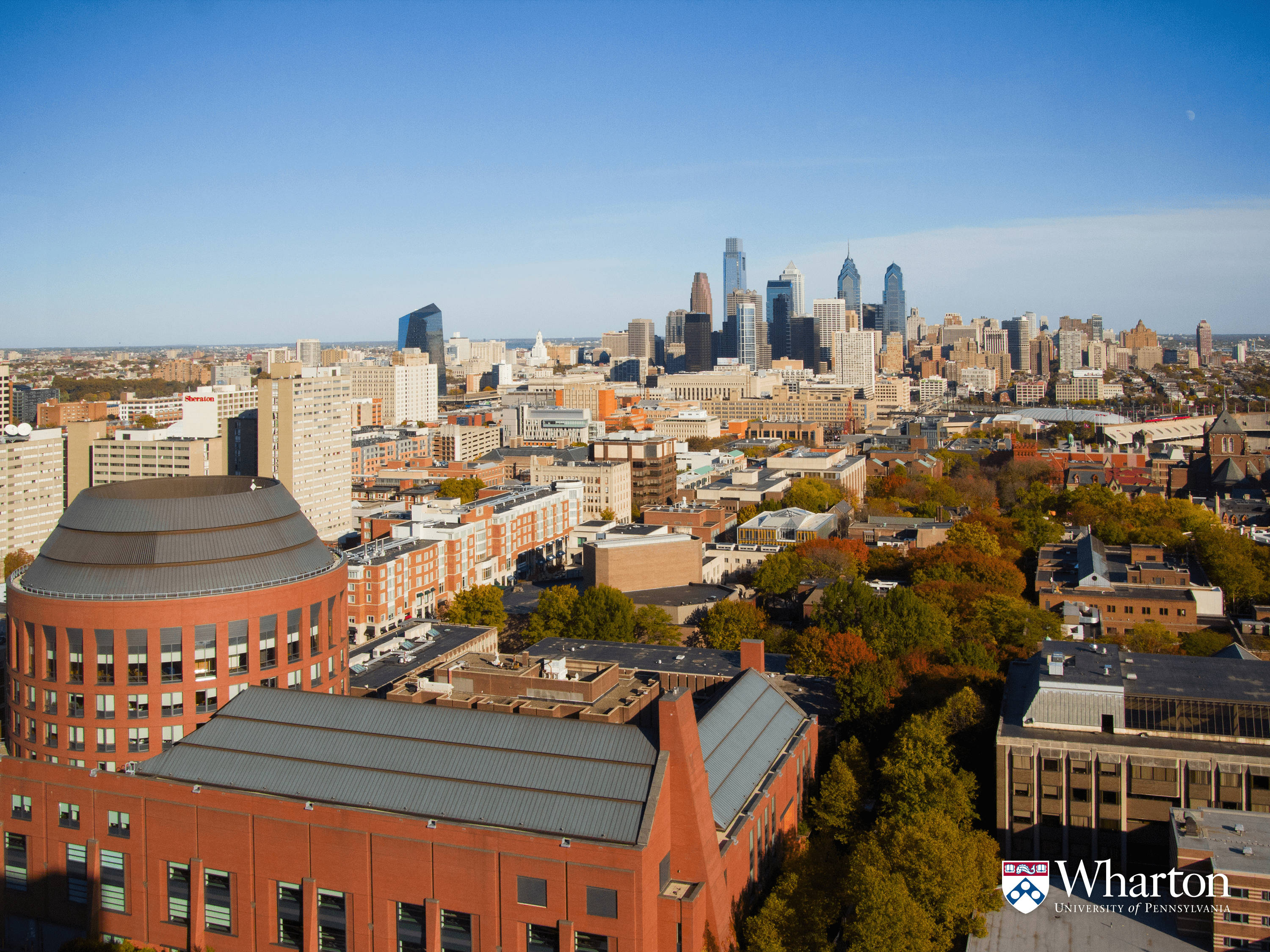 美學 桌布 壁紙 — Wharton School 校園的鳥瞰圖，秋樹和費城天際線在晴朗的藍天下。