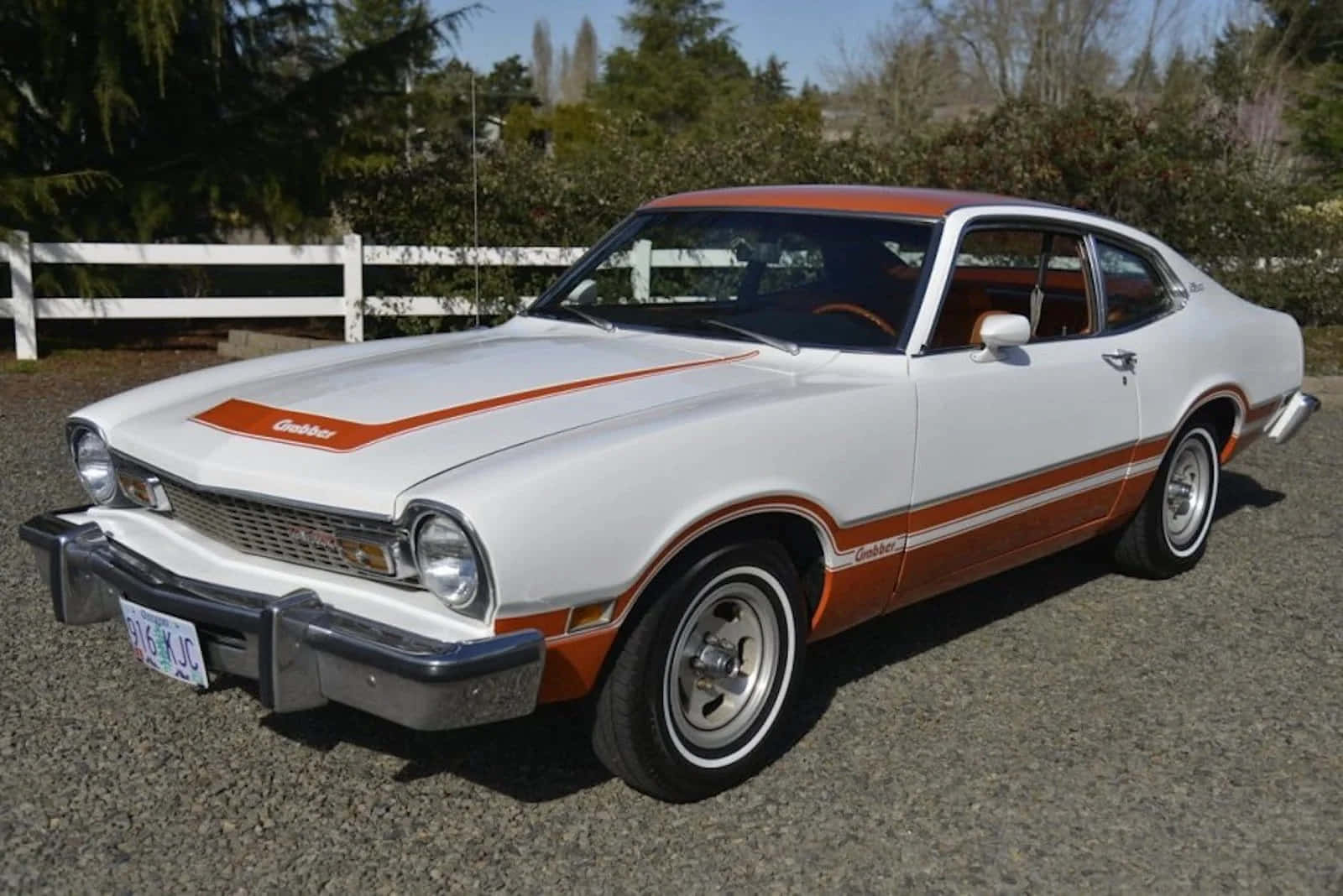 Ford Maverick 桌布 壁紙 — 一輛白色和橙色的經典雪佛蘭Chevelle，帶有鍍鉻保險桿，停在白色柵欄附近的礫石上。