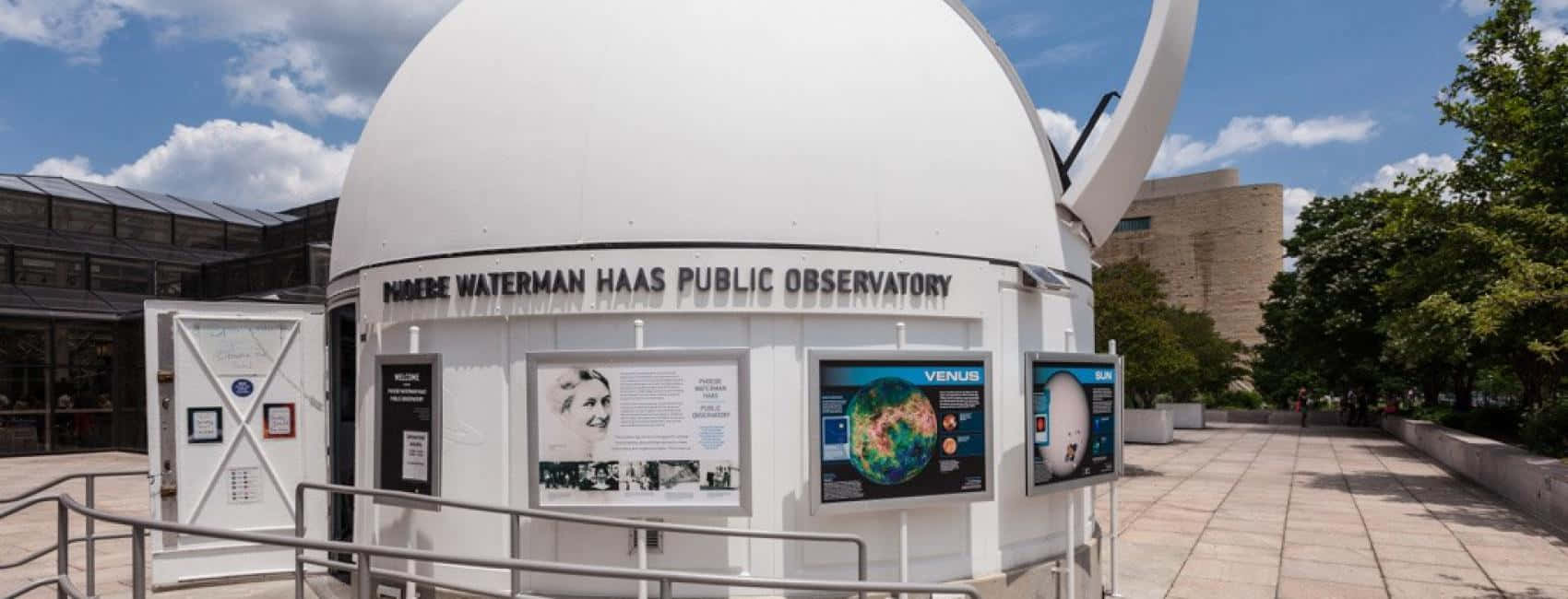 Observatory 桌布 壁紙 — 一個白色圓頂天文台，帶有開放的狹縫和教育展板，矗立在晴朗的藍天和白雲之下。