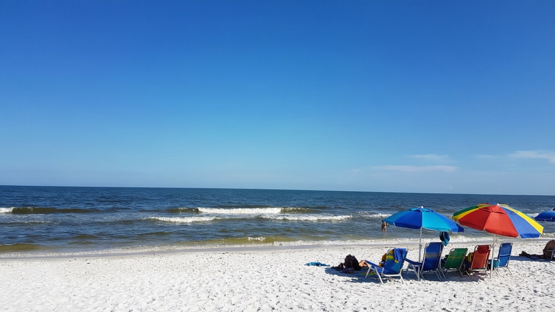Florida Beach Bliss 壁紙 — 白色沙灘，色彩繽紛的遮陽傘和椅子，在清澈的藍天下，靠近溫柔的海浪。