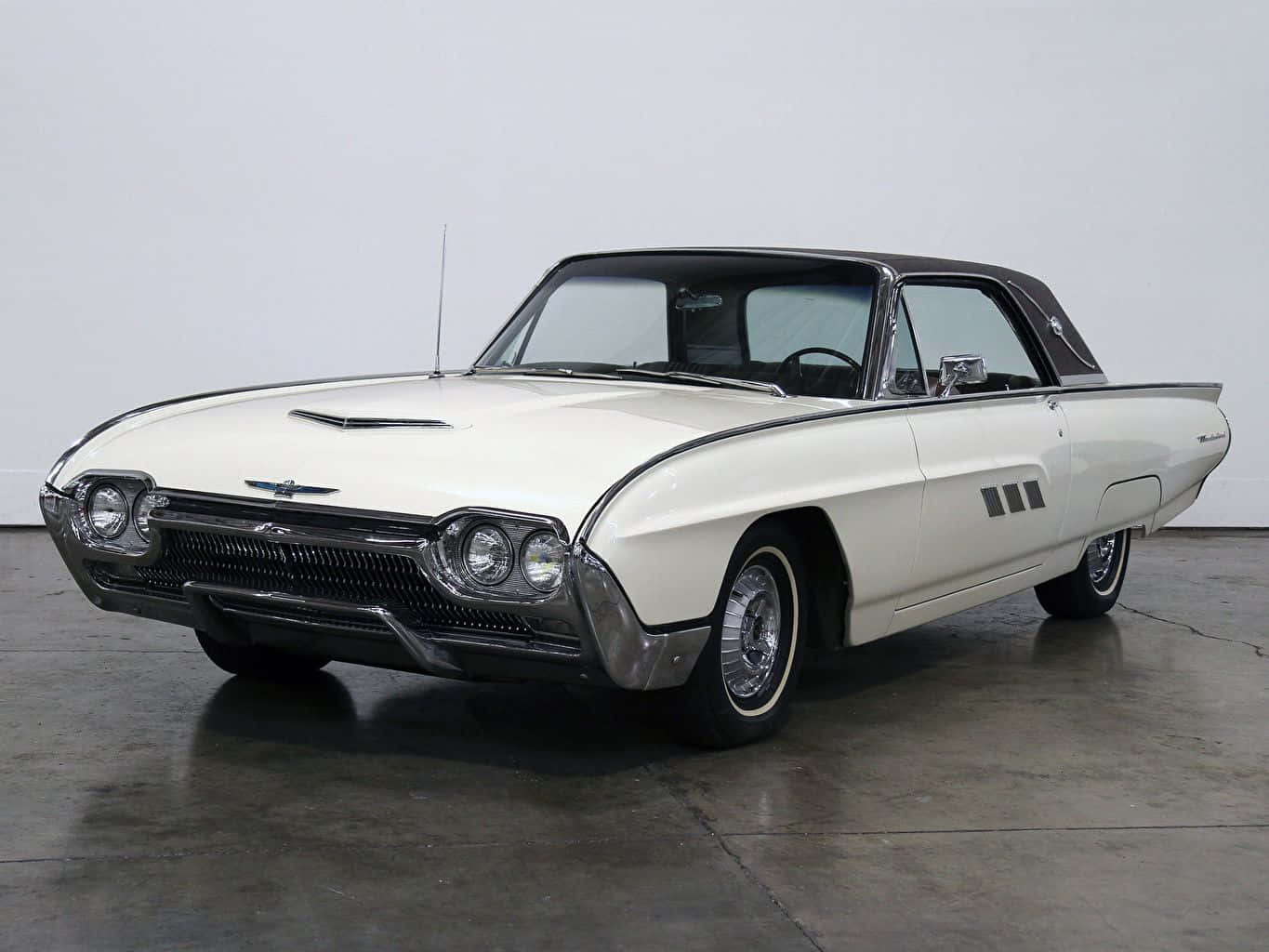 Ford Thunderbird 桌布 壁紙 — 一架純白色的1960年代福特雷鳥敞篷車，配備黑色車頂和鍍鉻裝飾，矗立在簡約的攝影棚空間中。