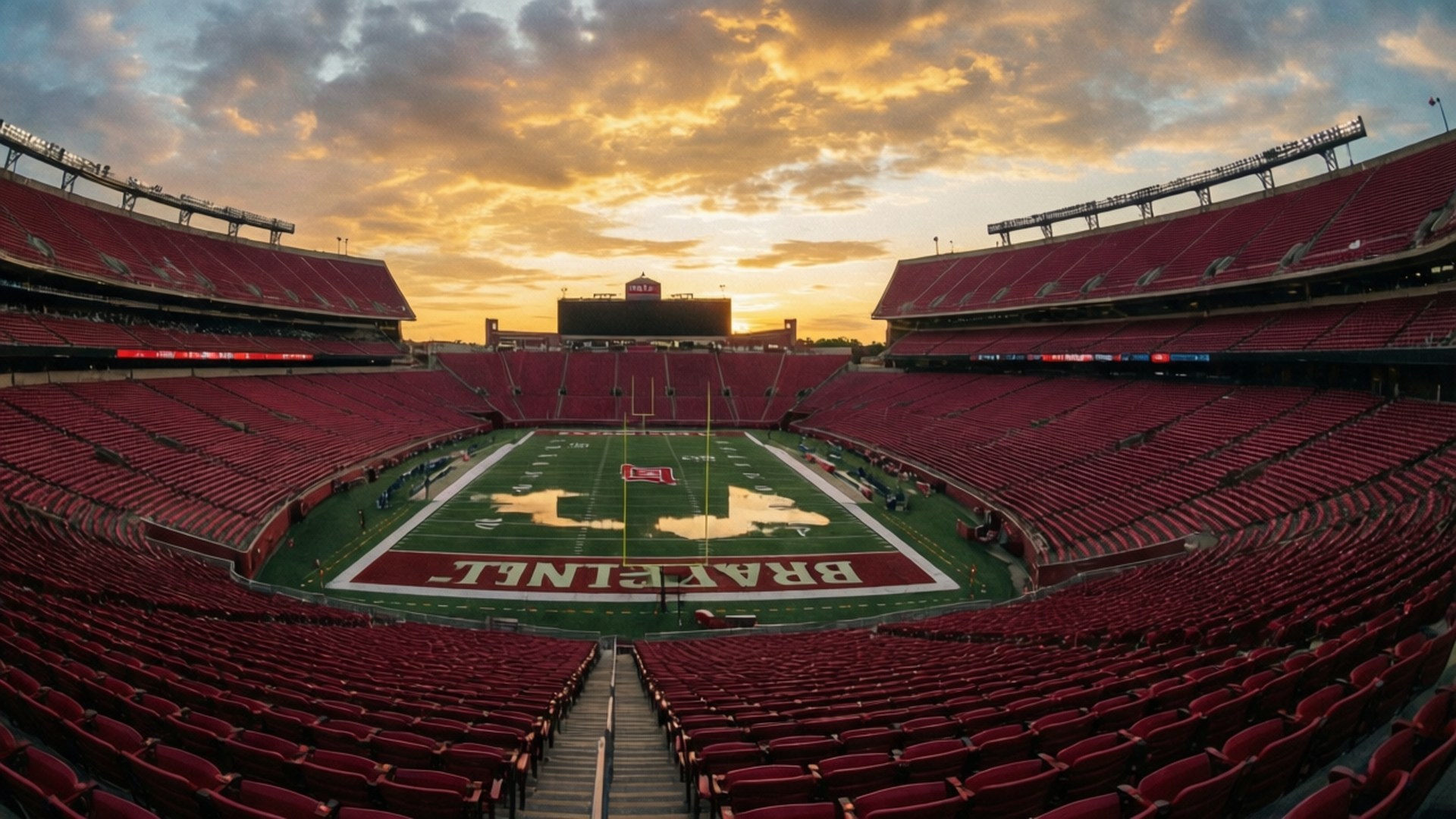 Stadium Sunset 壁紙 — 日落時分空無一人的足球場廣角視角，紅色座位和綠色球場上以白色字母顯示「BRAZIL」。